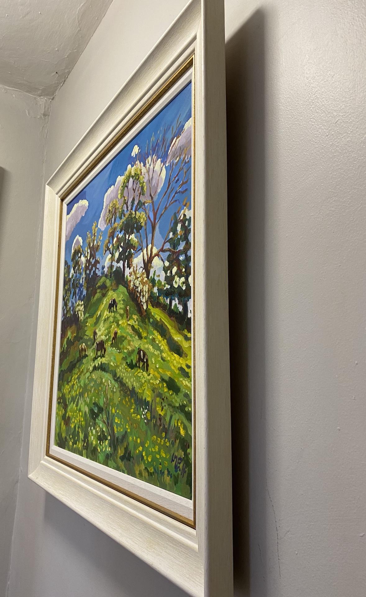 Grazers on the Motte and Bailey ist ein Original-Ölgemälde von Lucy Pratt. Es zeigt eine schöne Landschaft mit grünen Hügeln, grasenden Kühen, hohen Bäumen und blauem Himmel im Hintergrund. Ein helles und schönes englisches
