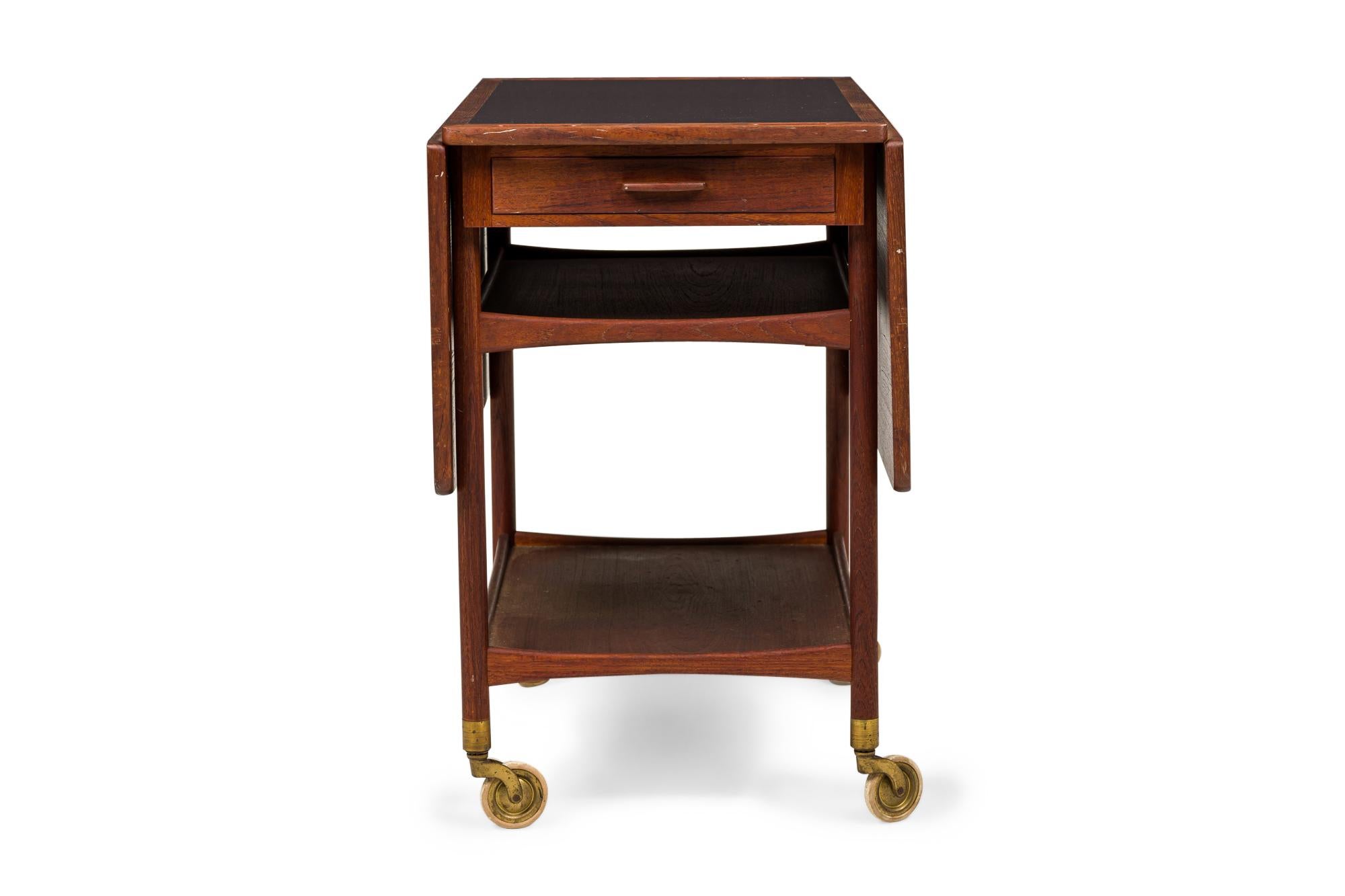 Danish Mid-Century rectangular two-tier serving trolley with a teak frame, an inset black laminate top, and two teak drop leaves, resting on four casters. (LUDVIG PONTOPPIDAN)(Similar piece: DUF0231)
