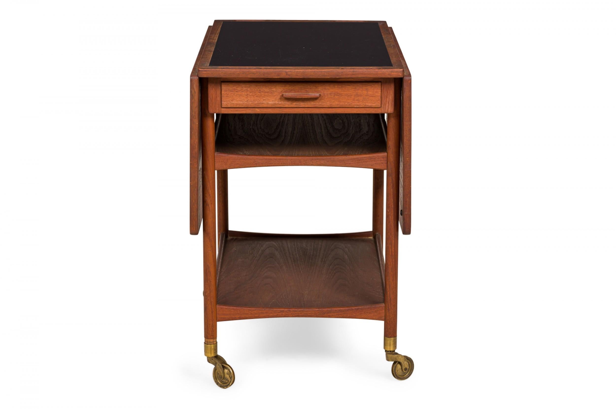 Danish Mid-Century rectangular two-tier serving trolley with a teak frame, an inset black laminate top, and two teak drop leaves, resting on four casters. (LUDVIG PONTOPPIDAN)(Similar piece: DUF0230)
