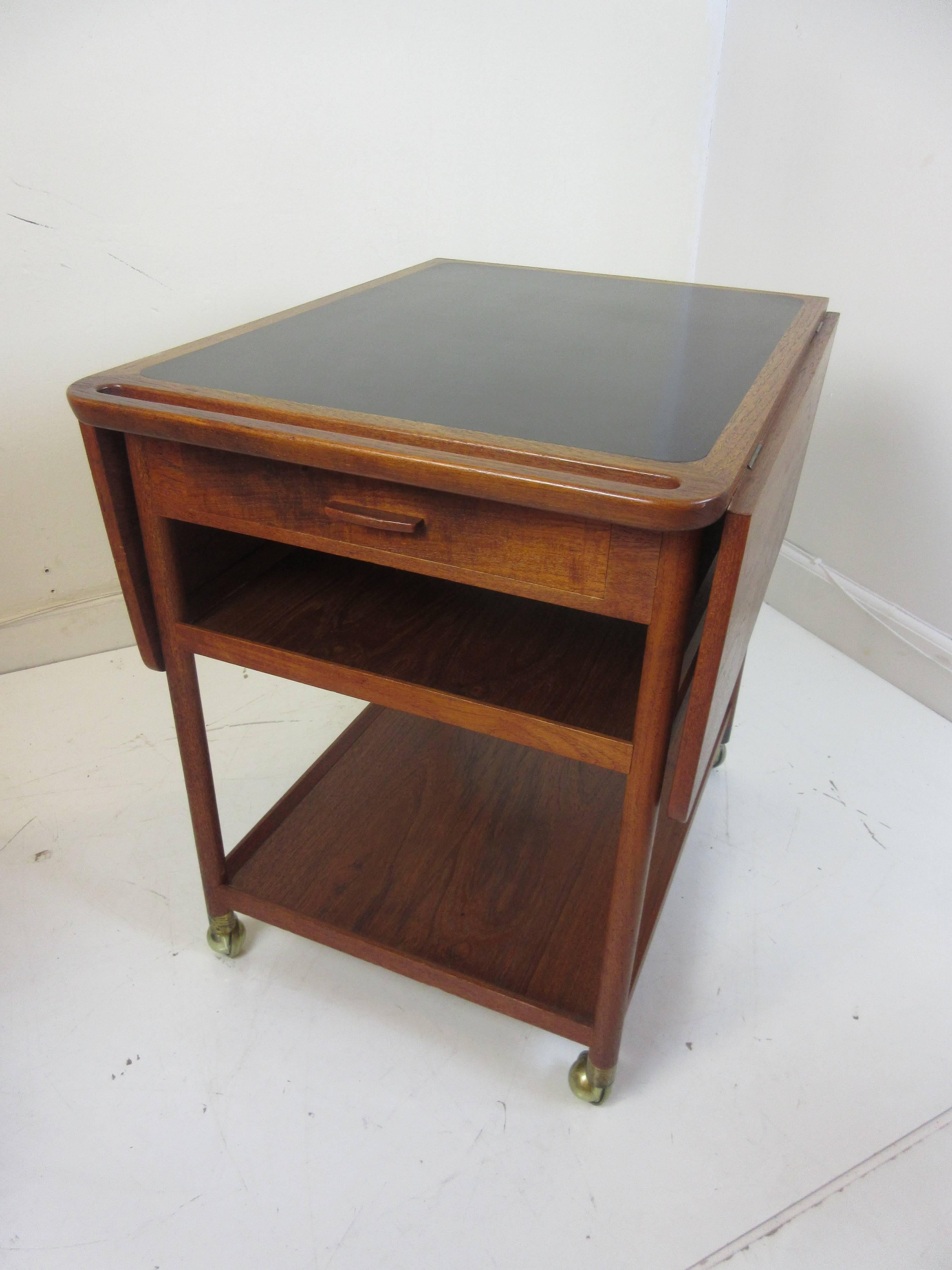 Ludvig Pontoppidan teak tea cart with two 11 inch drop leaves, one drawer and three shelves with the top shelve covered in black laminate. Bottom of drawer has the original makers decal.