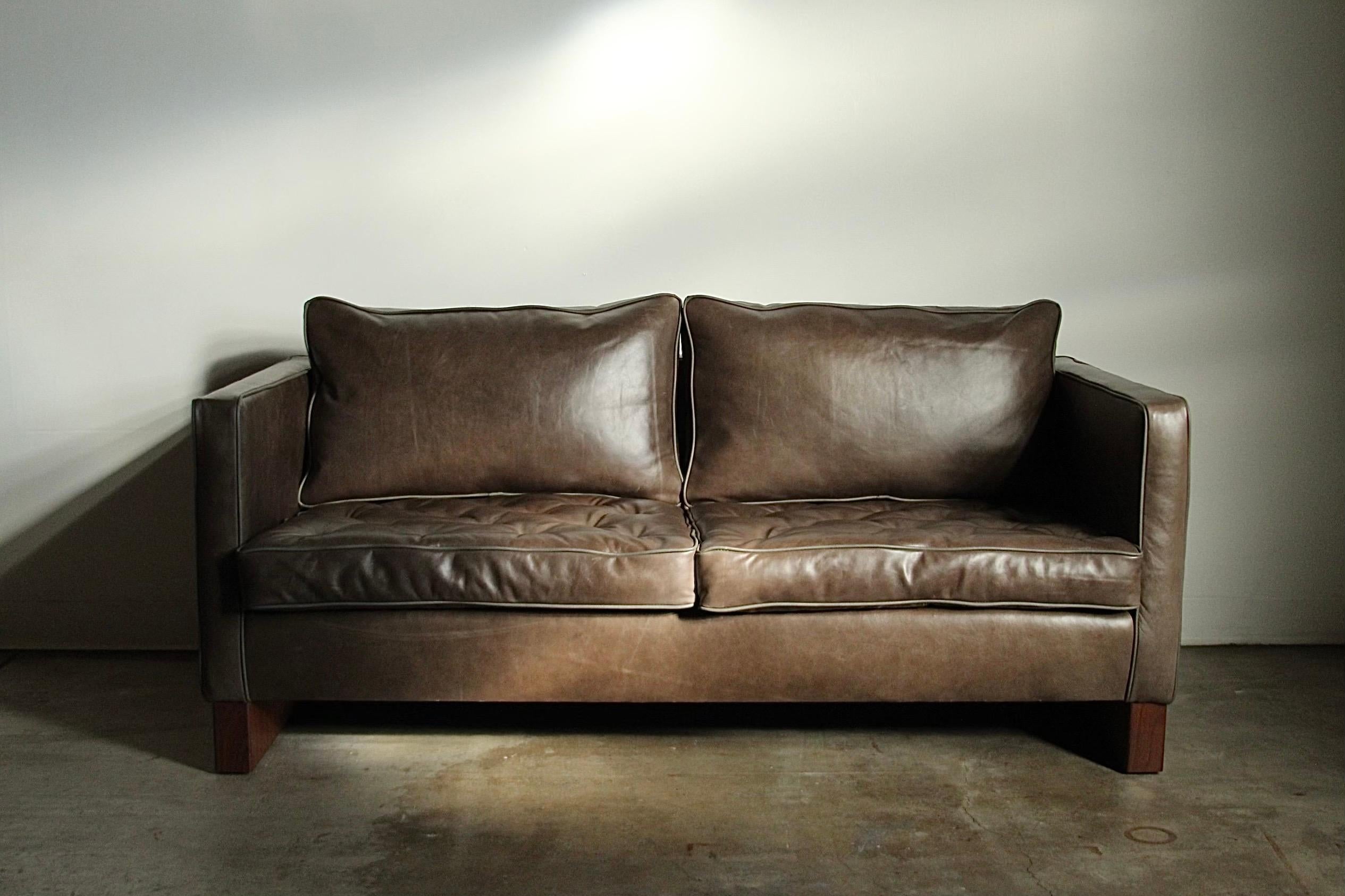A solid and very uncommon cube form loveseat sofa designed by Ludwig Mies van der Rohe and manufactured by Knoll in the 1970s. This striking, sturdy sofa is freshly upholstered in beautifully distressed gray-green leather and sits on two profound