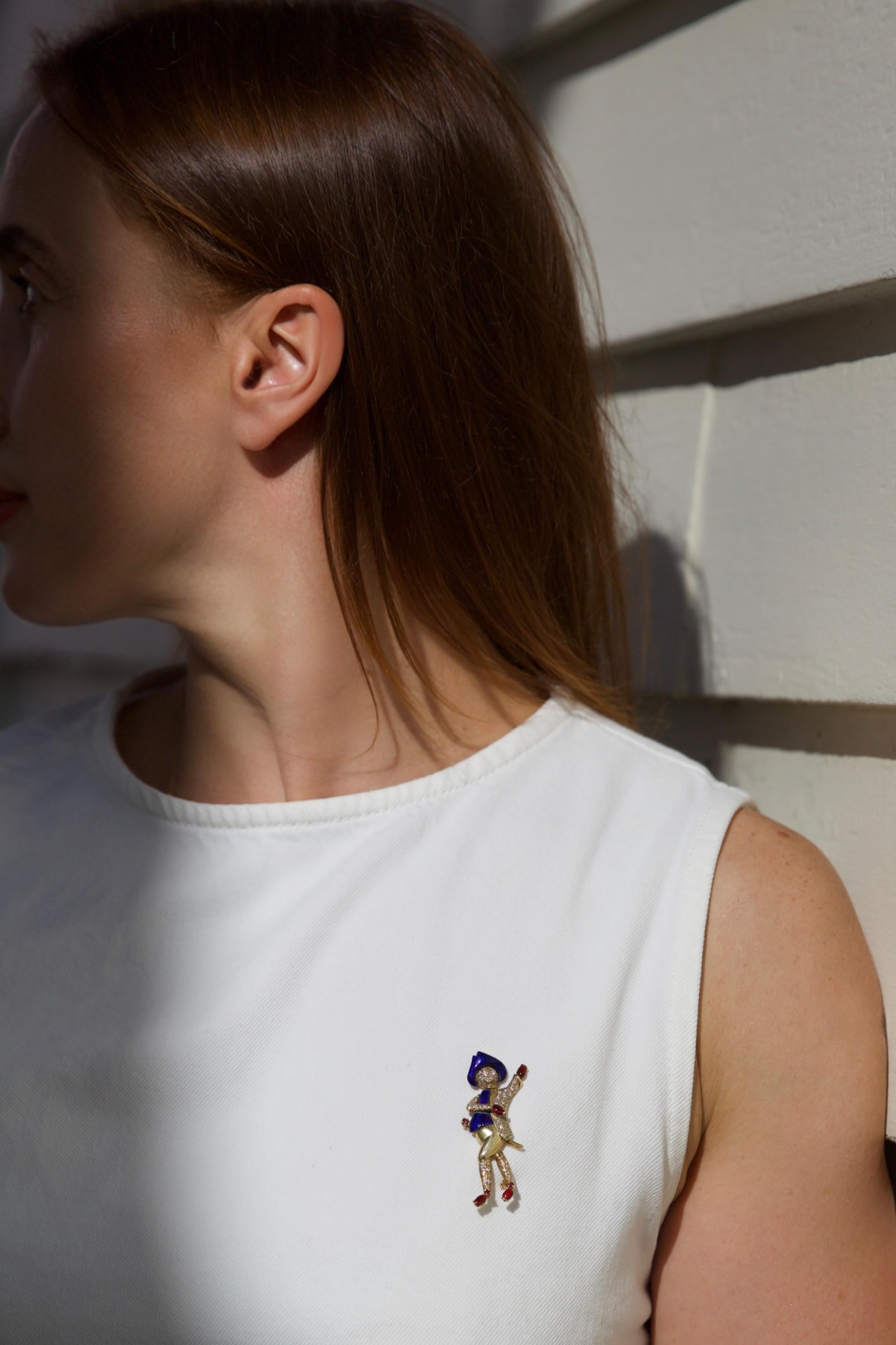 Eine figurale Brosche aus 18kt Gelbgold im Stil von Ludwig Müller. Die Brosche zeigt einen Mann im Kostüm, der mit blauer Emaille, Diamanten und Rubinen verziert ist.

Abmessungen -
Gewicht: 13 g
Höhe: 5.6 cm
Breite: 1.6 cm

Spezifikationen
Stil: