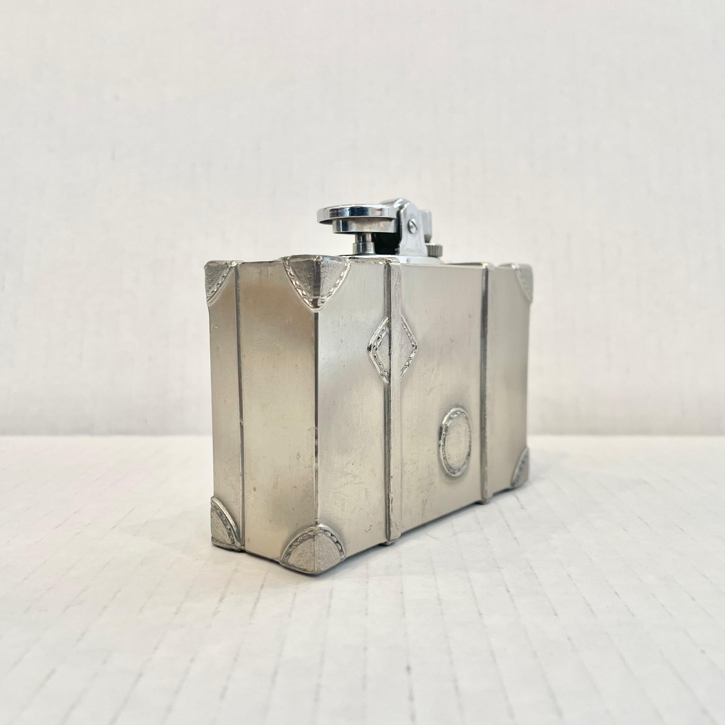 Cool vintage table lighter in the shape of a luggage trunk with straps and bag tags. Made completely of metal with a hollow body. Light patina giving this piece a classic silver color. Cool tobacco accessory and conversation piece. Working lighter.