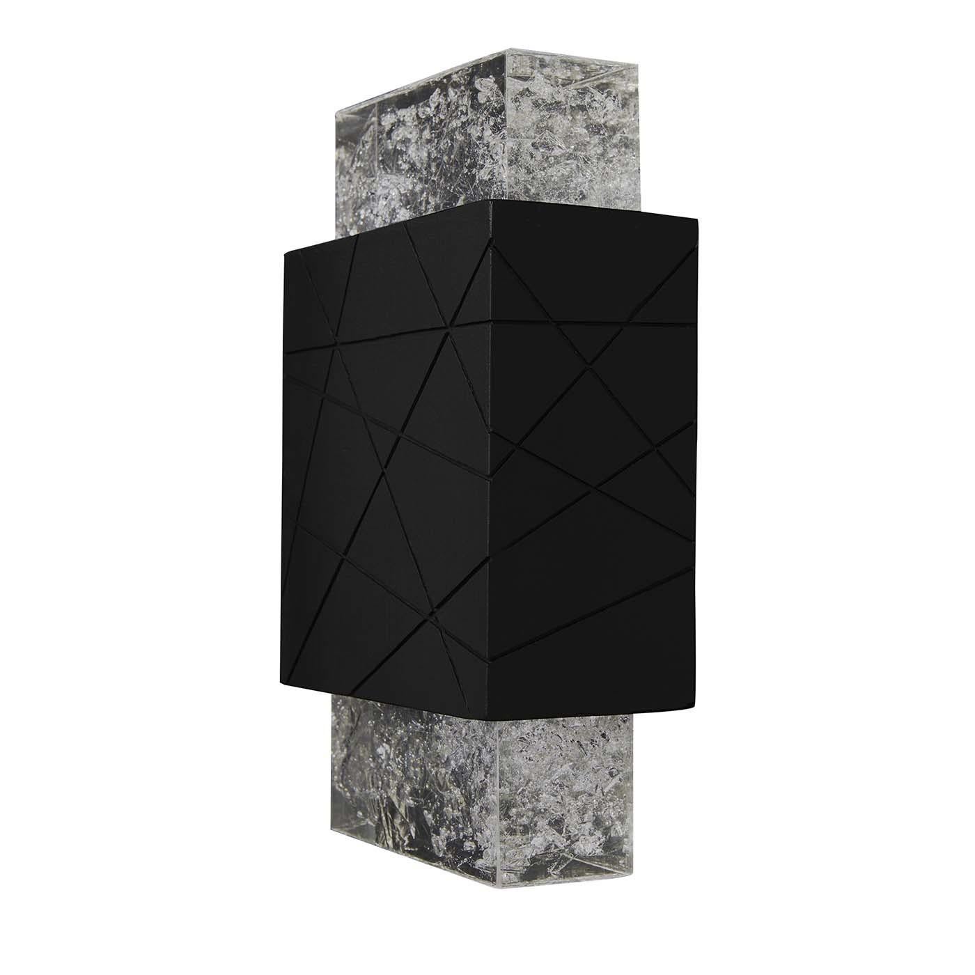 Light, architectural space and natural materials are the main elements of this wall lamp that merges geometric volumes and transparency in a stern yet stylish design. Handcrafted of black volcanic rock, the central body is engraved with irregular