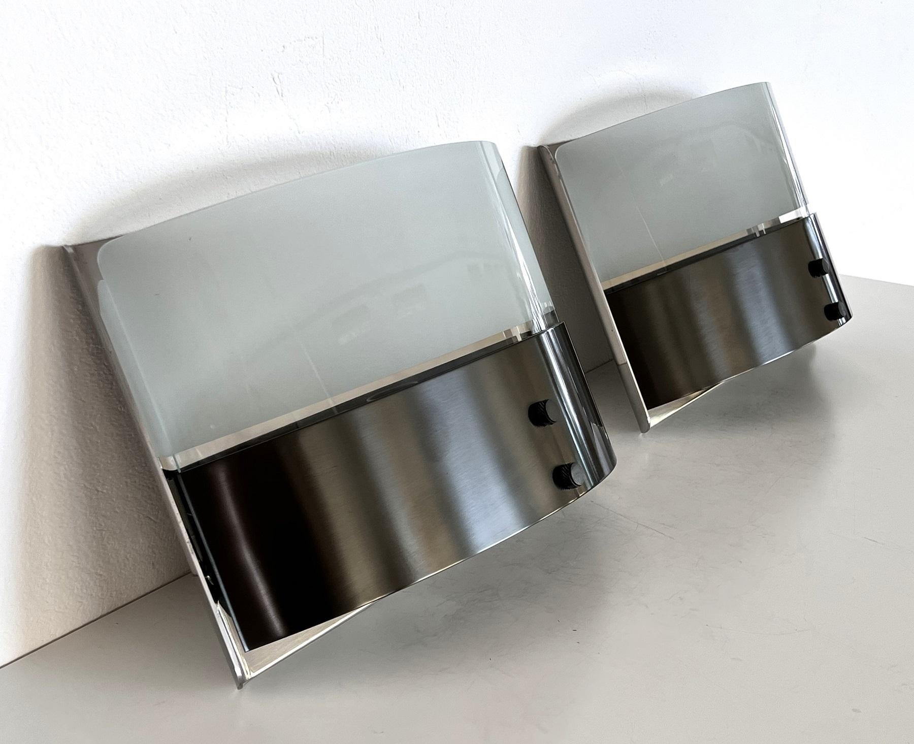 Fantastic pair of strong and heavy wall sconces, designed from Luigi Caccia Dominioni in 1979 and produced from Azucena in the 80s.
The wall sconces are made of gorgeous shiny stainless steel wall bracket and curved glass lampshades with partial