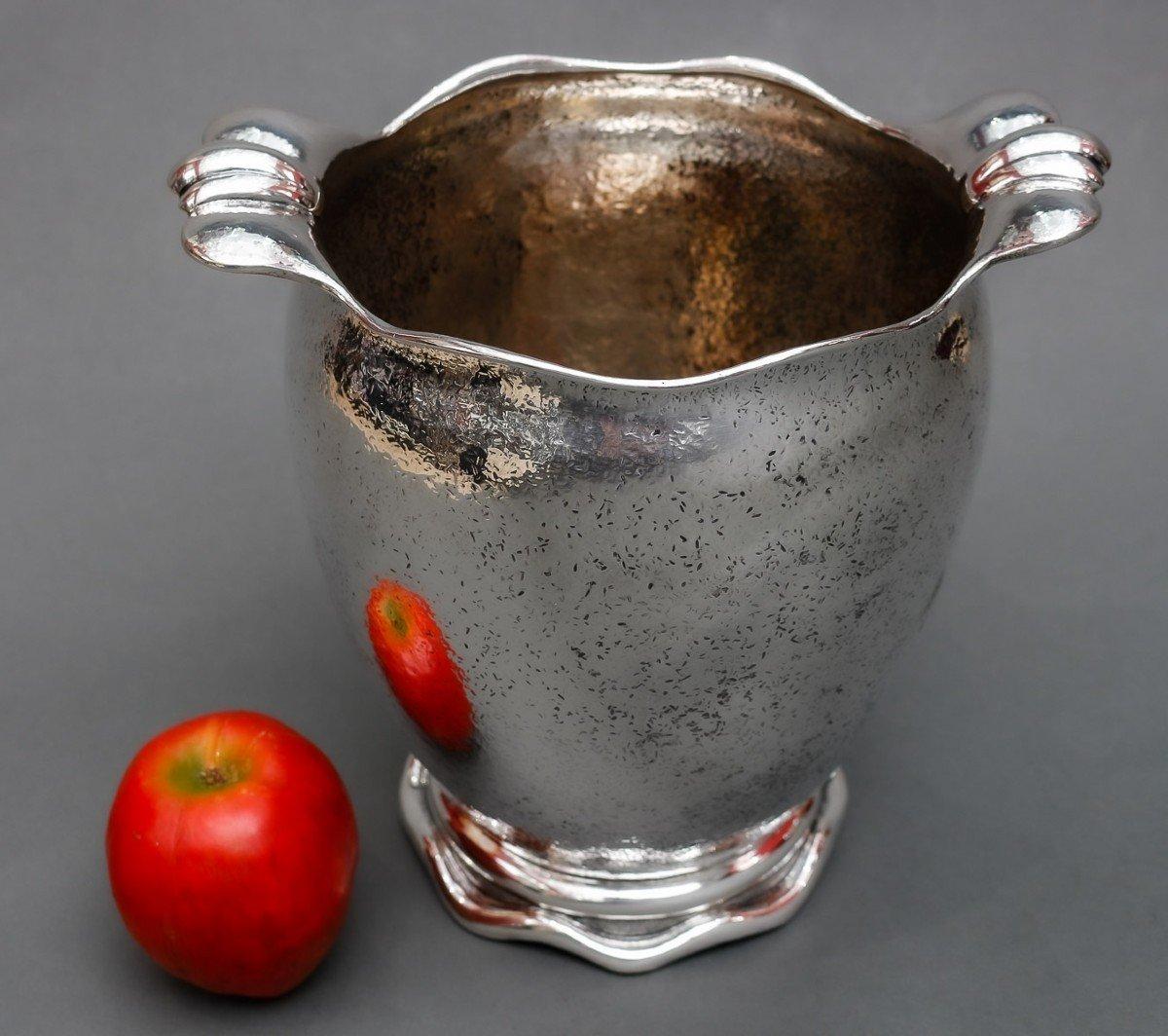 Solid silver cooler placed on a wavy pedestal, the body is swollen and flanked at the neck by adjoining ear handles. Granite appearance, hammer mounted, vermilion interior.

Dimensions: height 23 cm – width at the handles 23.5 cm

Material: Silver