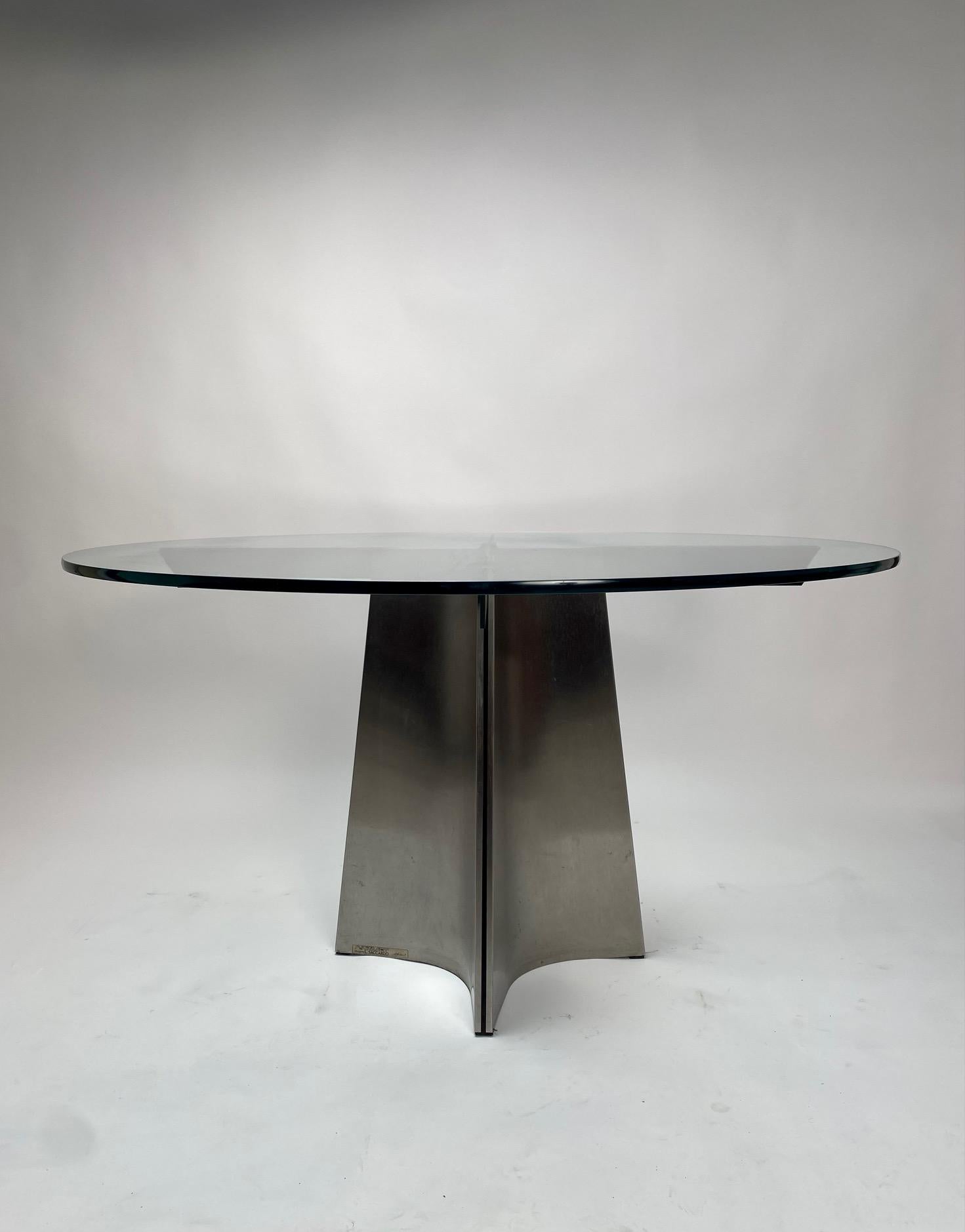Round table by Luigi Saccardo for Maison Jansen - Arrmet, glass and aluminum, France/Italy, 1970s.

Round pedestal dining table in brushed aluminum. A circular clear glass top; the base is formed of four concave curved plates of metal, which