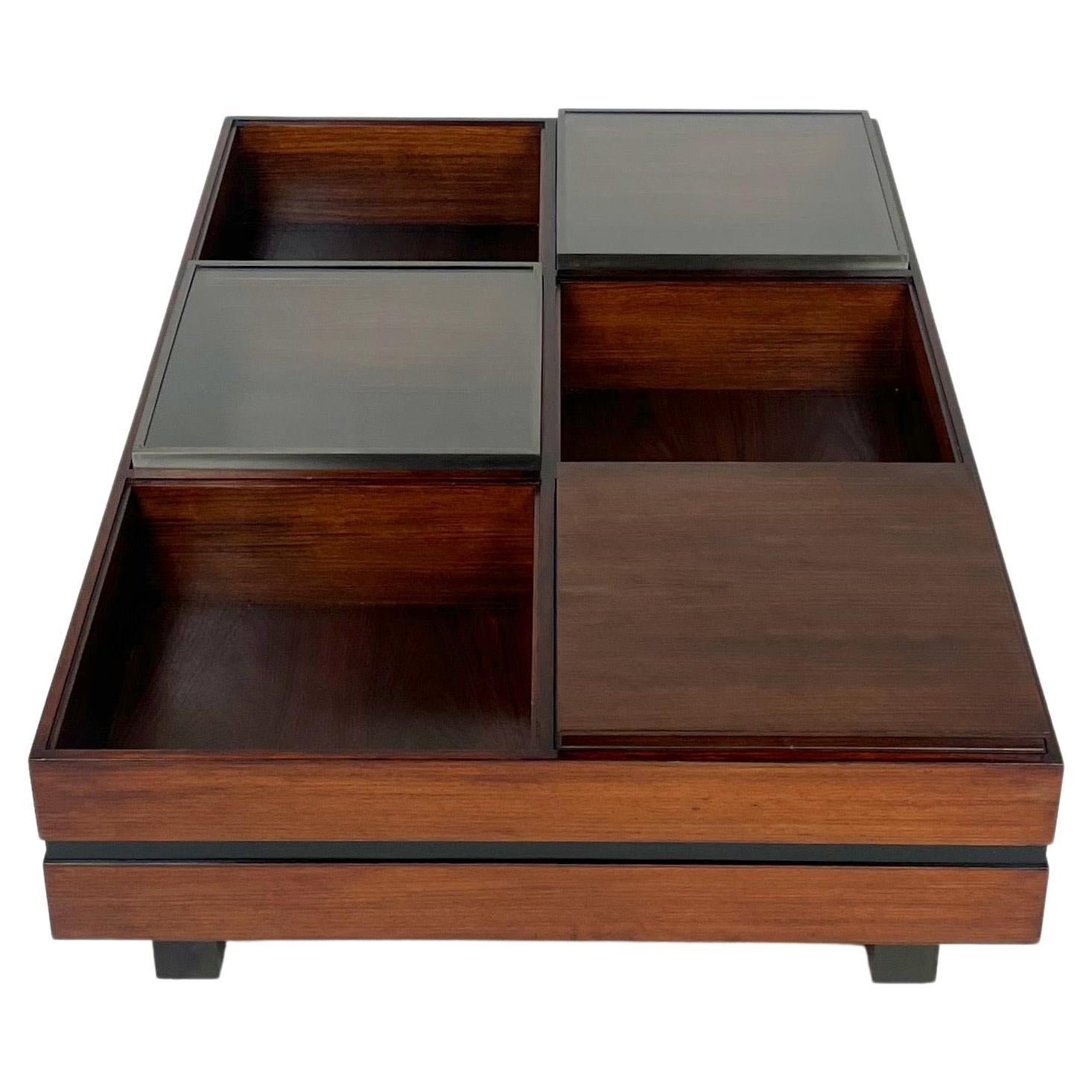 This modular rosewood, metal and glass coffee table produced by Luigi Sormani in the 1960s in Italy.

 Is divided into six different compartments: empty, removable tray, and glass lid. The sides are divided horizontally in half by a darker band,