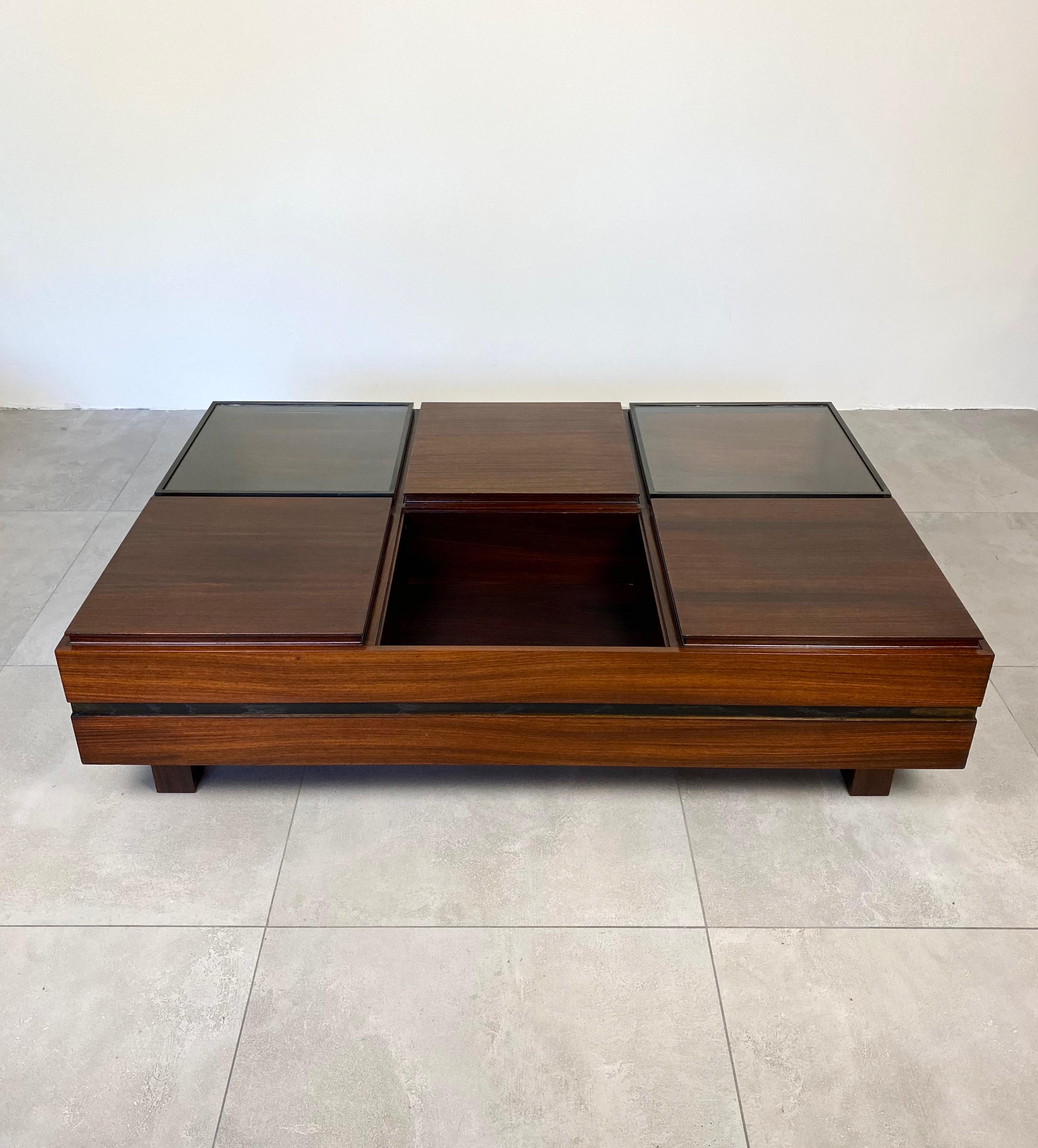 This modular rosewood coffee table produced by Luigi Sormani in the 1960s is divided into six different compartments: empty, removable tray, and glass lid. The sides are divided horizontally in half by a darker band, which lightens the profile of