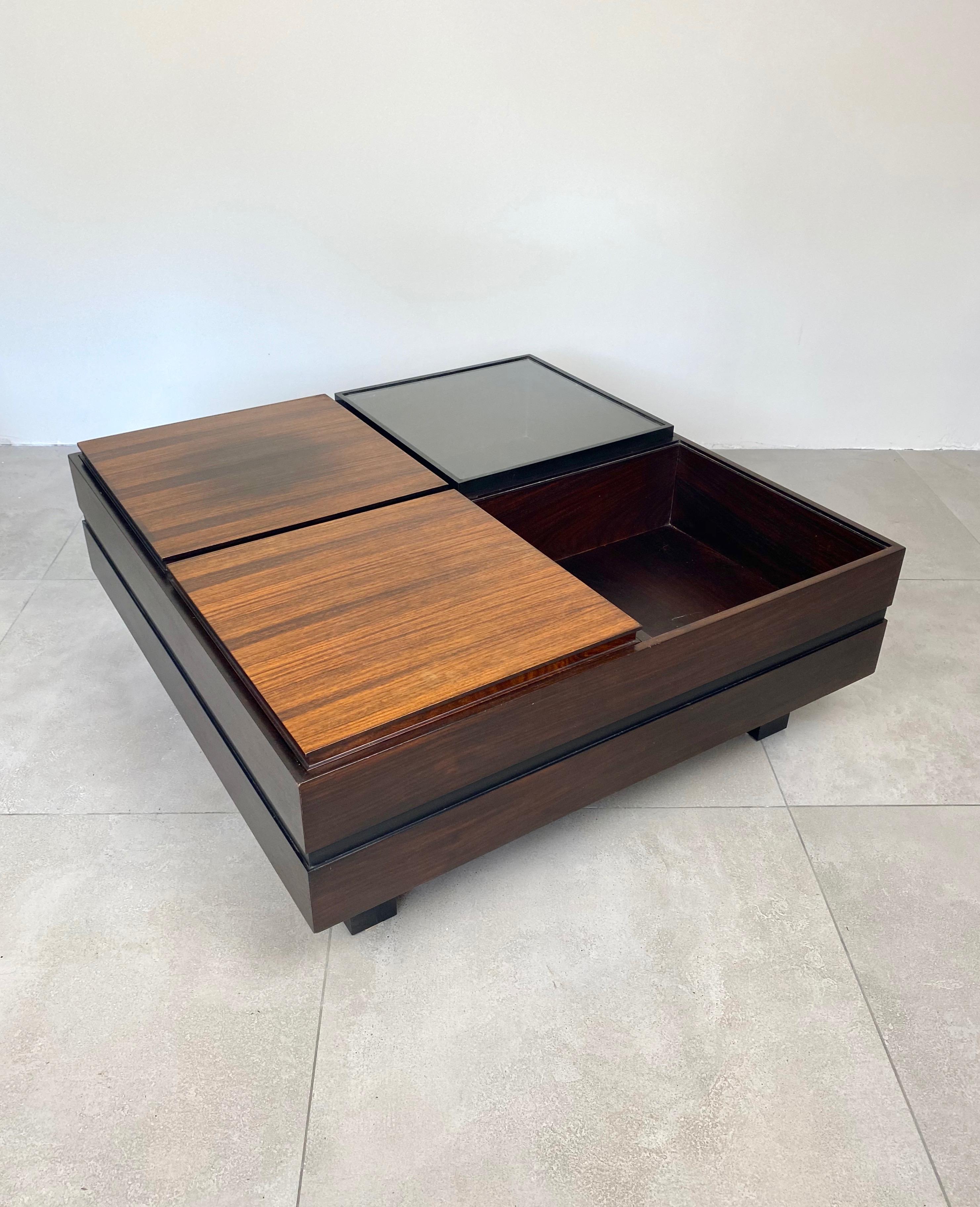 Cette table basse modulaire produite par Luigi Sormani dans les années 1960 est divisée en quatre compartiments ; l'un vide, un autre un plateau amovible, le dernier un couvercle en verre. Les côtés sont divisés horizontalement en deux par une bande