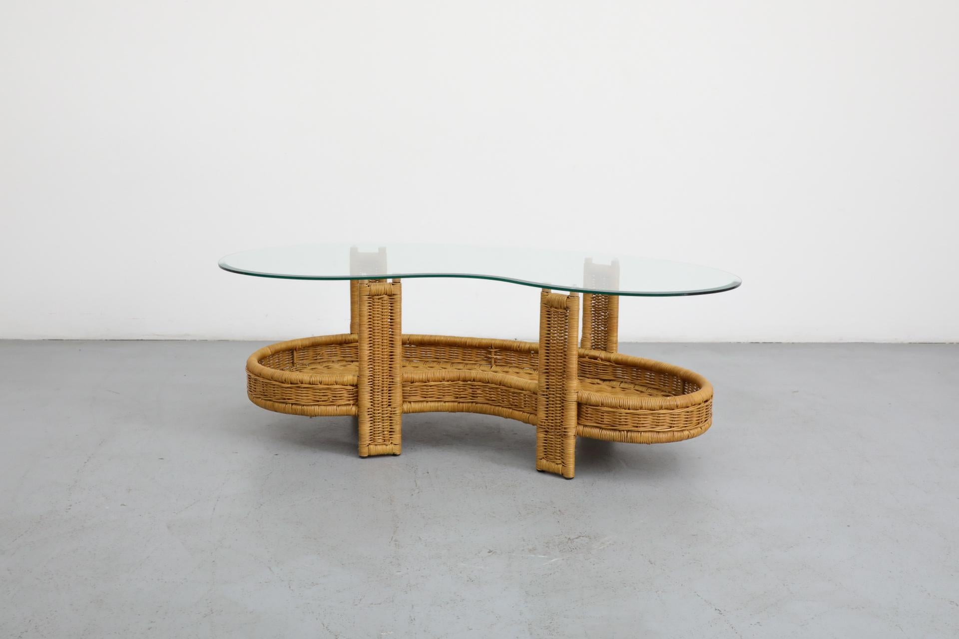 Kidney bean shaped rattan coffee table with lower magazine shelf and plate glass top. in original condition with visible wear consistent with its age and use. Shown with Tobia Scarpa inspired rattan high back lounge chair (LU922442538762) listed