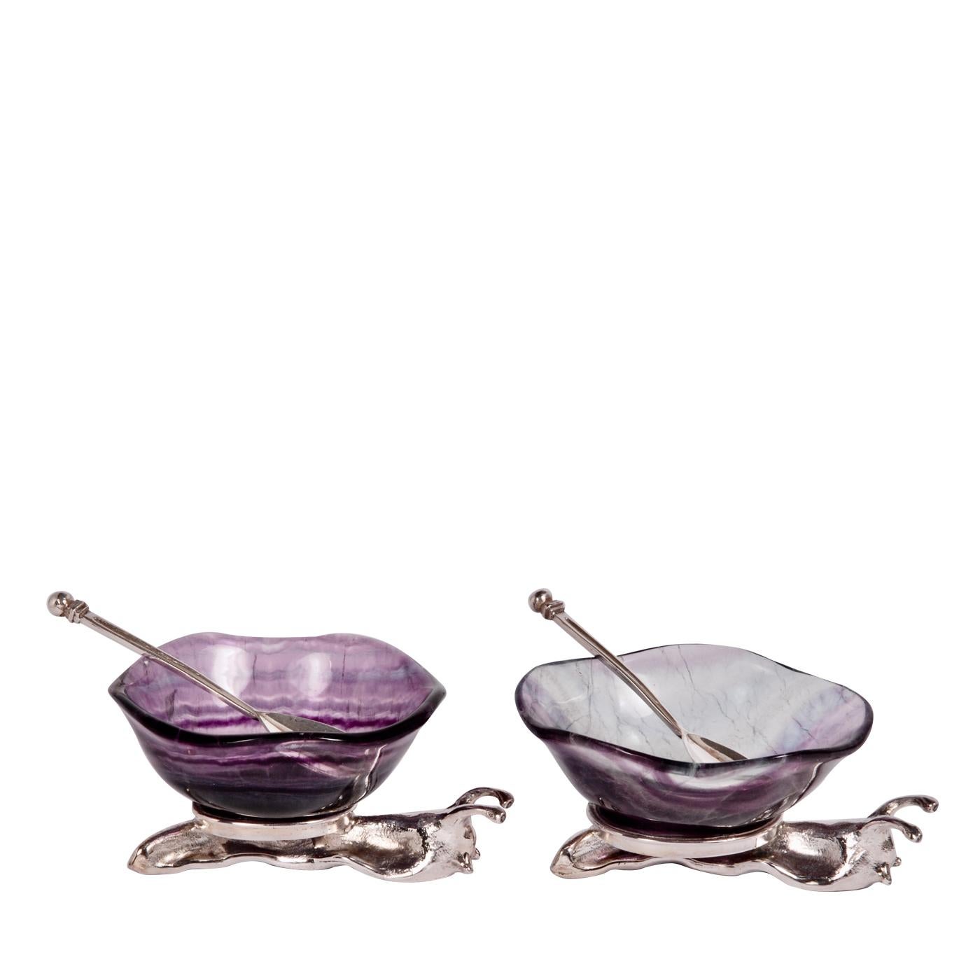 This eccentric set of salt and pepper cellars will bring an accent of unmistakable originality to any kitchen decor. Customizable in several shades, the two bowls in fluorite with irregular edges rest each on a snail-shaped base crafted of sterling