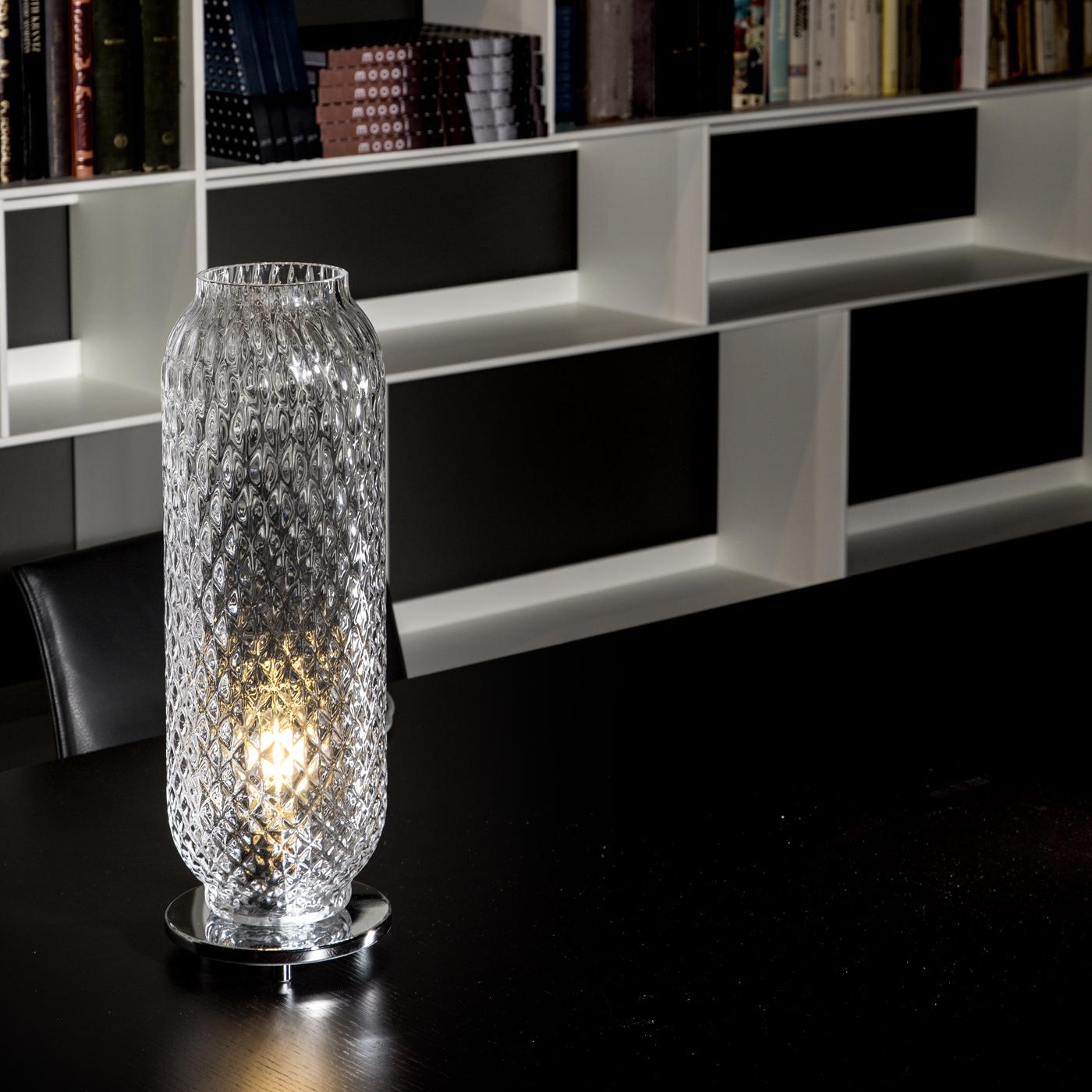 This elegant table lamp of the Lumè Collection transforms a Murano glass vase in a refined, timeless design. The clear blown glass diffuser has a cylindrical shape open on top and rests on a round polished chrome metal base. The exquisite bubbled