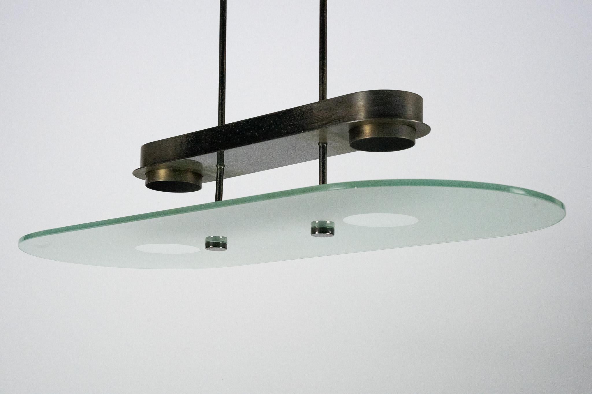Elegant Mid-Century chandelier by Lumi Milano, crafted in Italy during the 1970s. This sophisticated piece features a sleek brass structure with a distinctive curved design, supporting a large oval glass diffuser. The combination of warm brass tones