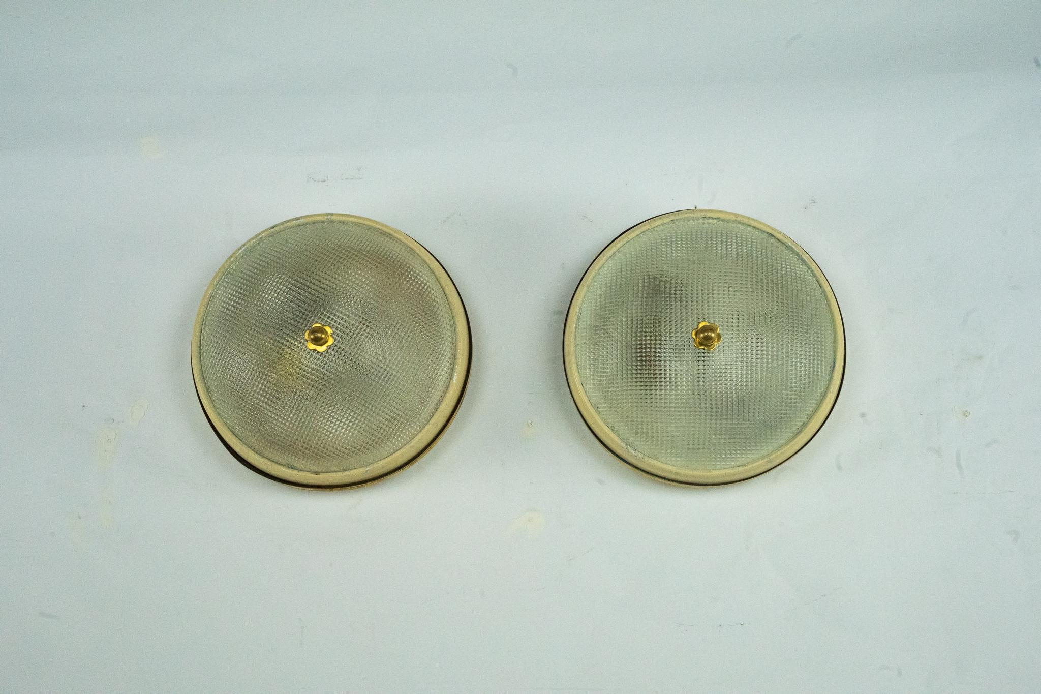 Pareja de lámparas de pared o techo fabricadas por Lumi Milano, Italia, años 50. Cada luminaria presenta una estructura de latón con acabado dorado y un difusor de cristal prensado, sujeto en el centro por un característico remate de latón. El