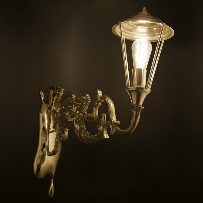 Drawing inspiration from the Victorian era, this antique fixture in polished gold plated brass with an intricate edge detailing arm topped by an elegant pane glass lantern hand-sculpted by a casting mold. Born from the rich tradition of iron forging