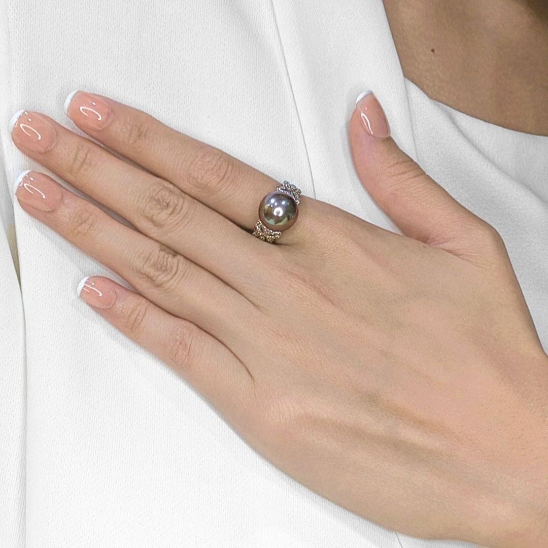 Schmücken Sie Ihre Hand mit der auffallenden Eleganz dieses exquisiten Rings, der sorgfältig aus strahlendem 18 Karat Weißgold gefertigt ist. Das Herzstück ist eine prächtige runde 11,99 mm große Perle, die in einem fesselnden grau-schwarzen Farbton