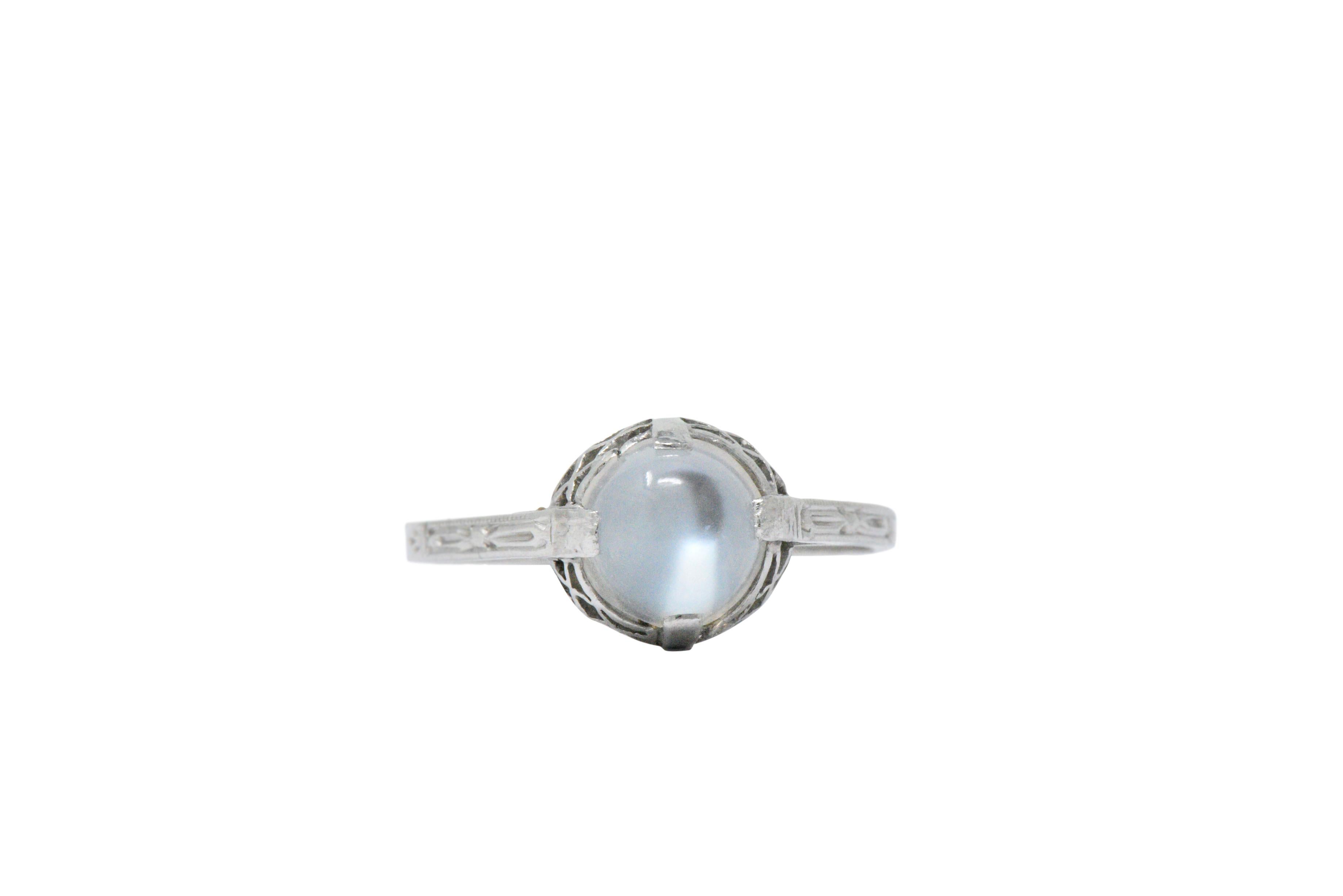 Centering a round cabochon moonstone measuring approximately 6.8 x 5.8 mm

Beautiful billowy light blue adularescence giving the ring an etherial feel

North, East, South, West setting with a pierced almost 