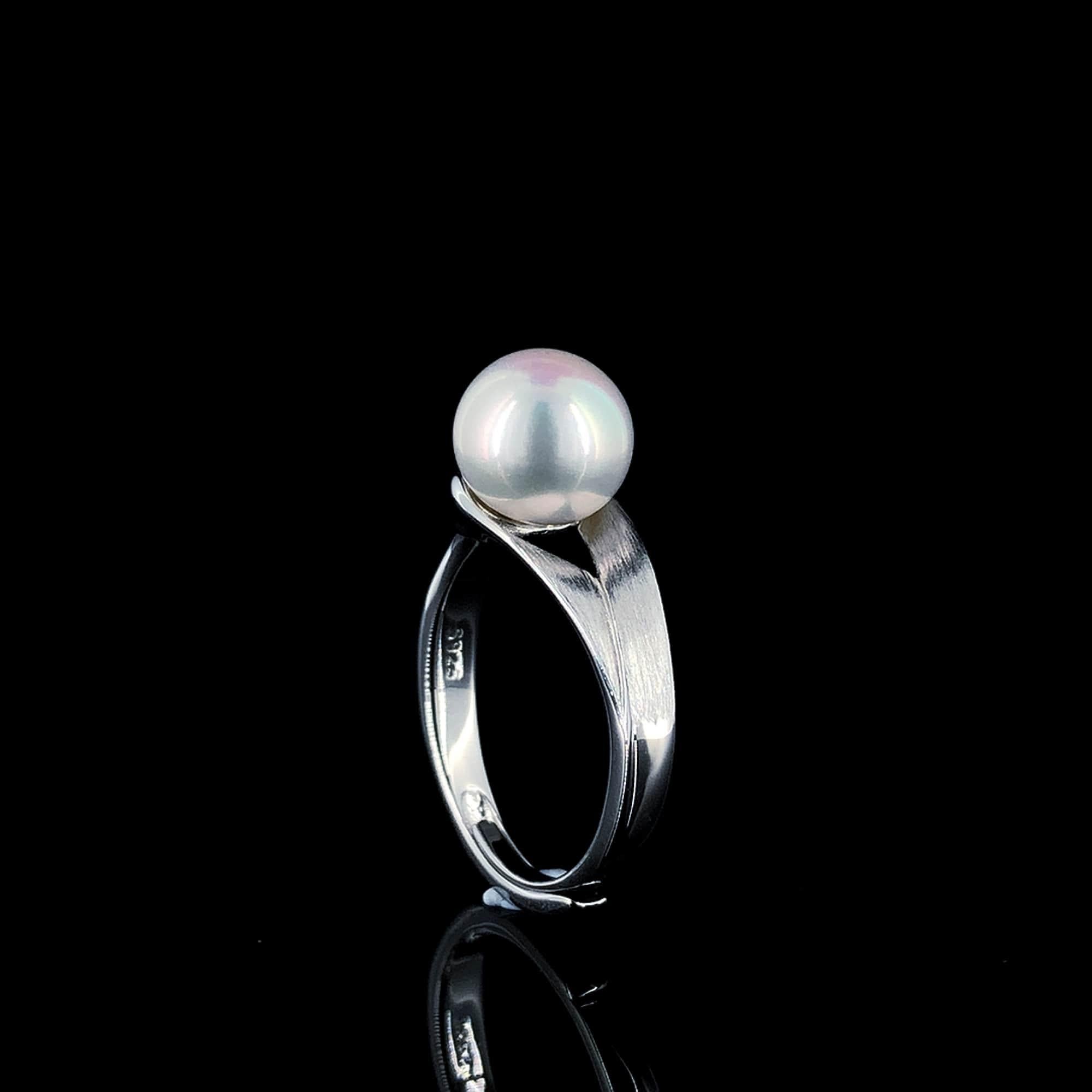 Ein bezaubernder Ring aus Sterlingsilber mit einer leuchtenden Süßwasserperle, die elegant auf dem Ring thront. Das strukturierte Band, ein Symbol für die komplizierte Reise des Lebens, umarmt die Perle zärtlich und verkörpert eine poetische