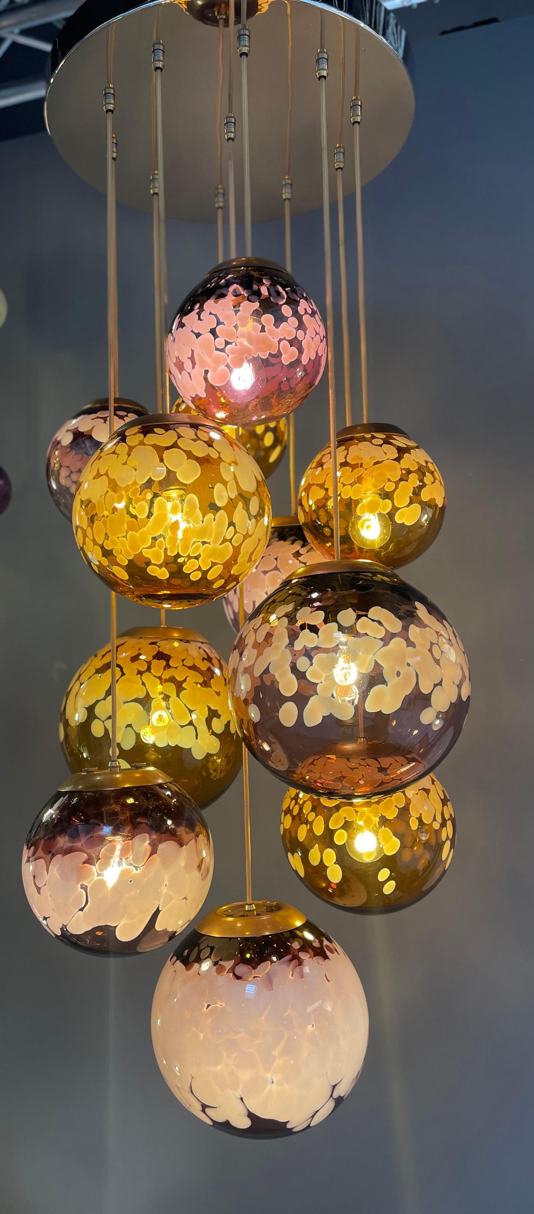 Il s'agit d'un lustre LUNA conçu par Karen Walker de Roast Designs et composé de 11 pendentifs en verre soufflé illuminés individuellement. Les pendentifs mesurent 20 cm, 25 cm et 30 cm de large et sont soufflés au Royaume-Uni. Le lustre est conçu