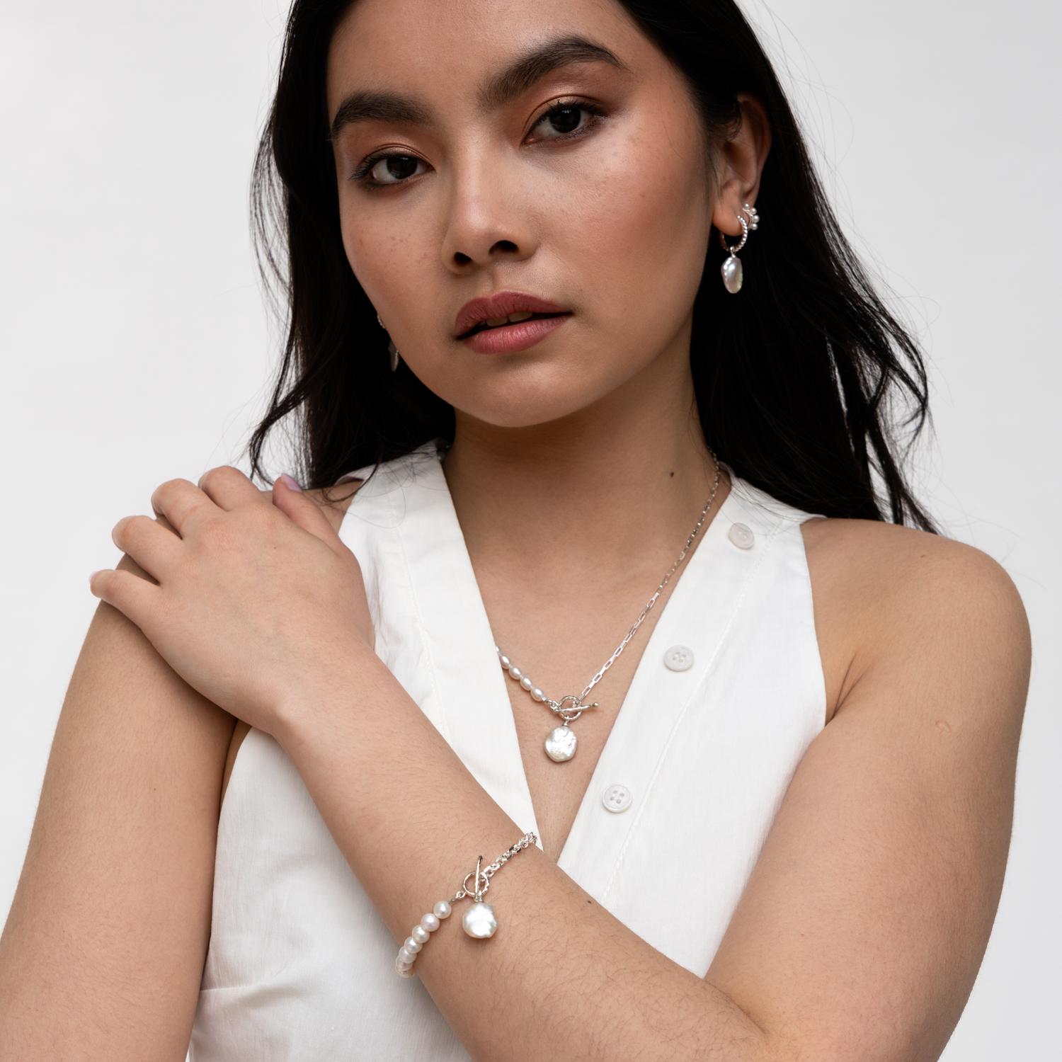 A playful modern take on a classic Dower & Hall design, this eclectic Luna Pearls bracelet combines 6mm round freshwater pearls and sterling silver rectangular link chain to dramatic effect. Accented with a 12 x 10mm keshi pearl drop, it fastens