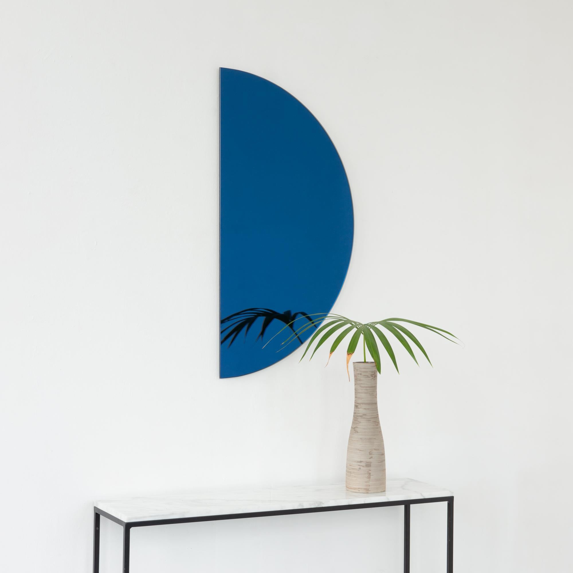 Minimalist half-moon Luna™ blue tinted frameless mirror with a floating effect. Fitted with a quality and ingenious hanging system for a flexible installation in 4 different directions. Designed and made in London, UK. 

Our mirrors are designed