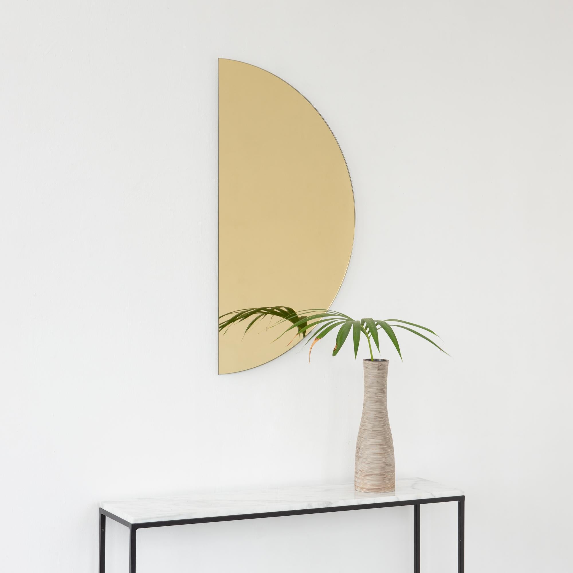 Minimalist half-moon Luna™ gold tinted frameless mirror with a floating effect. Fitted with a quality and ingenious hanging system for a flexible installation in 4 different directions. Designed and made in London, UK. 

The backing has a brand new