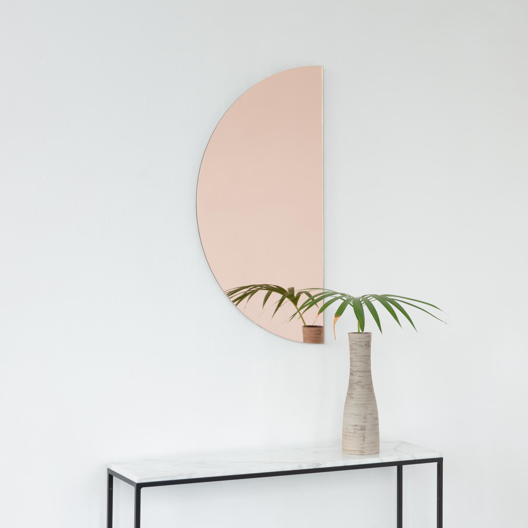 Minimalist half-moon rose gold (peach) tinted frameless mirror with a floating effect. Fitted with a quality and ingenious hanging system for a flexible installation in 4 different directions. Designed and made in London, UK. 

The backing has a