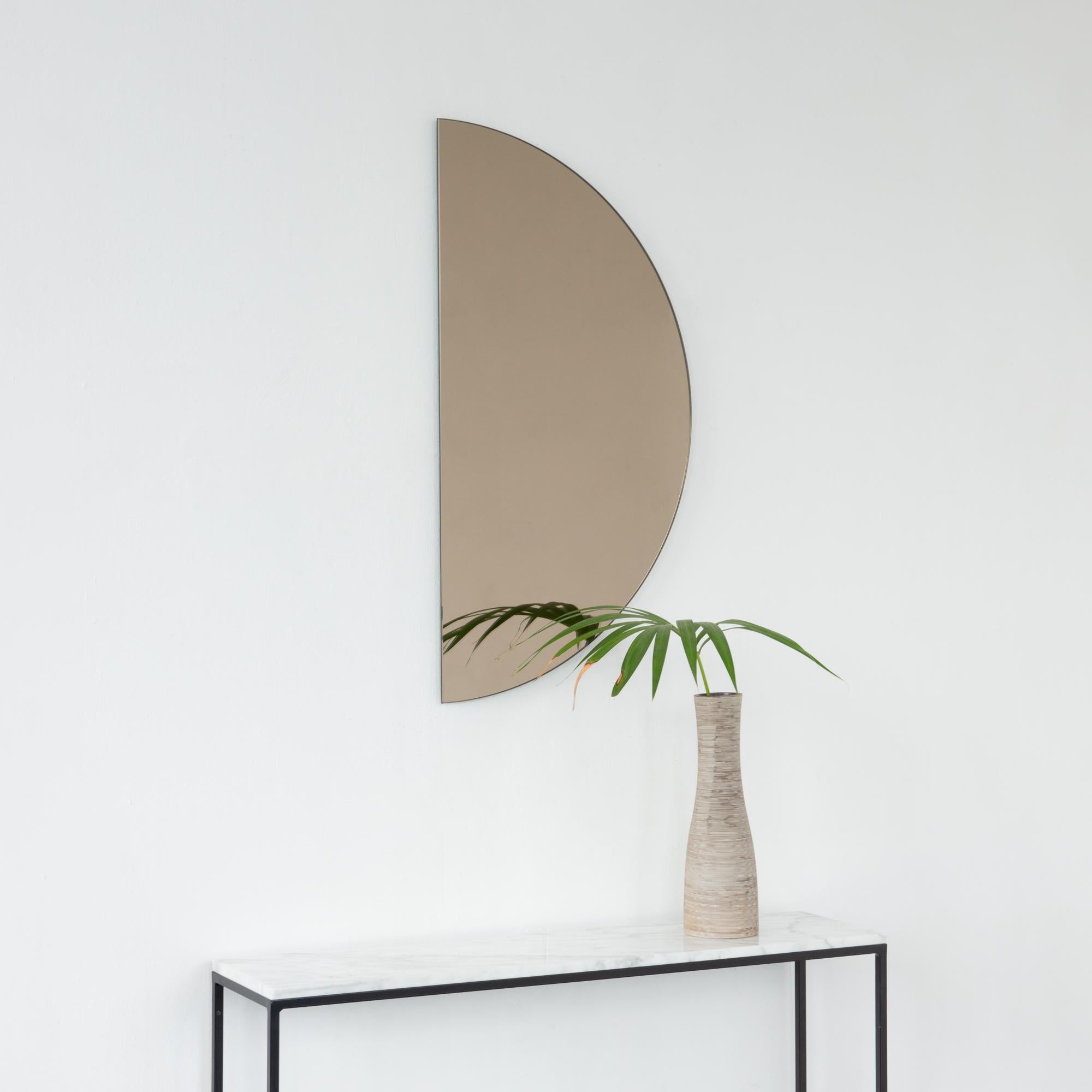 Minimalistischer, halbmondförmiger, rahmenloser Spiegel Luna™ in Bronze mit Schwebeeffekt. Ausgestattet mit einem hochwertigen und ausgeklügelten Aufhängesystem für eine flexible Installation in 4 verschiedenen Richtungen. Entworfen und hergestellt