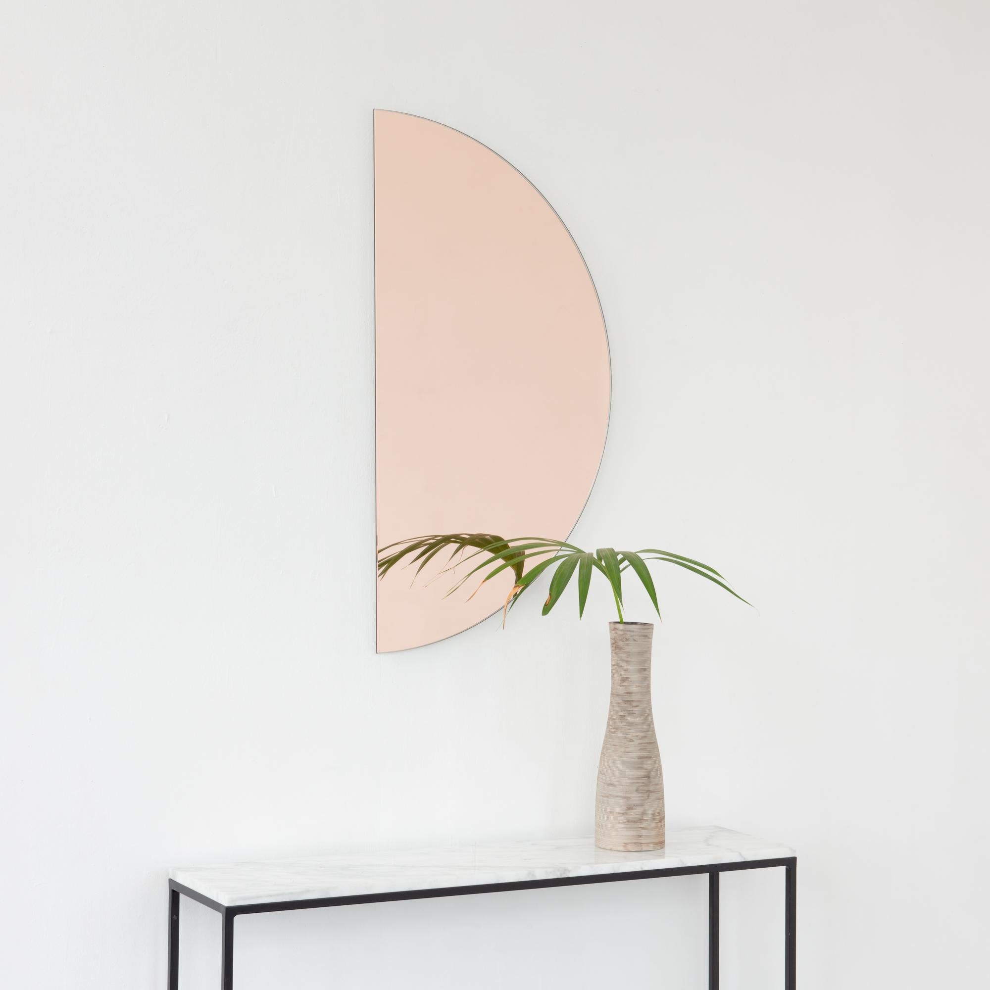 Minimalist half-moon rose gold (peach) tinted frameless mirror with a floating effect. Fitted with a quality and ingenious hanging system for a flexible installation in 4 different directions. Designed and made in London, UK. 

The backing has a