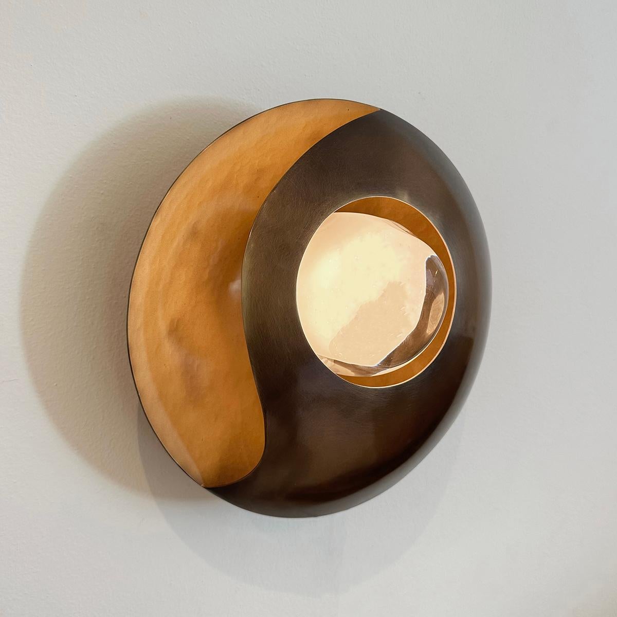 The Luna wall light’s simple round shape is elevated by its elliptical cross-section and distinctive cut-outs that let out a soft glow. At the center is our Sfera glass handblown in Murano. Shown with a satin brass interior and bronzo nuvolato