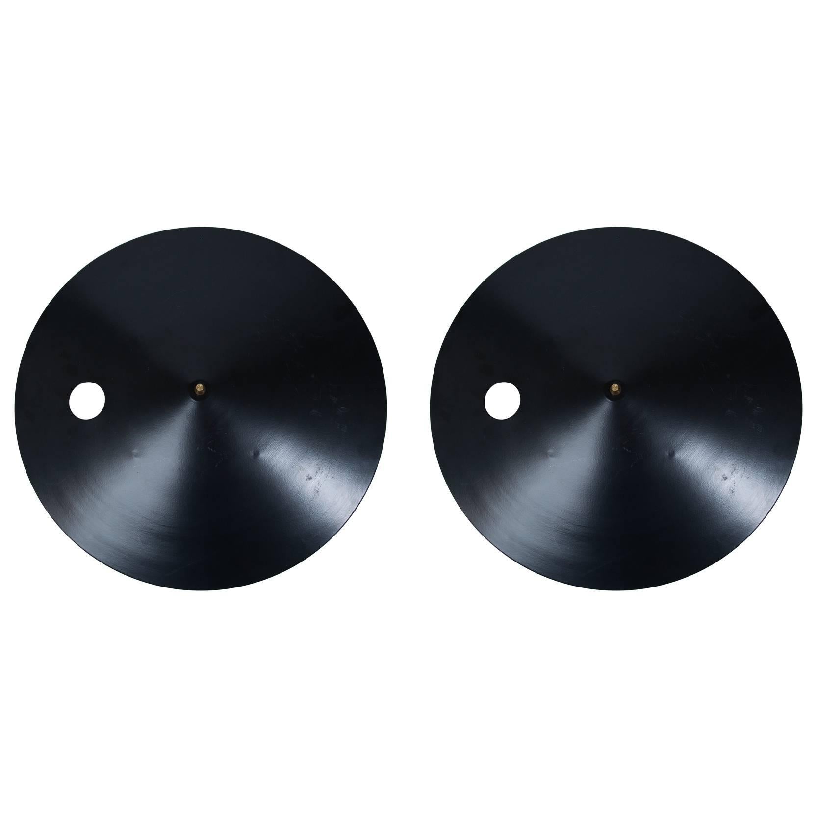 Pair of circular black enameled steel wall sconces with brass finials. Illumination exquisitely comes from the sides and a small cut-out circle on the shade. White enameled interiors.