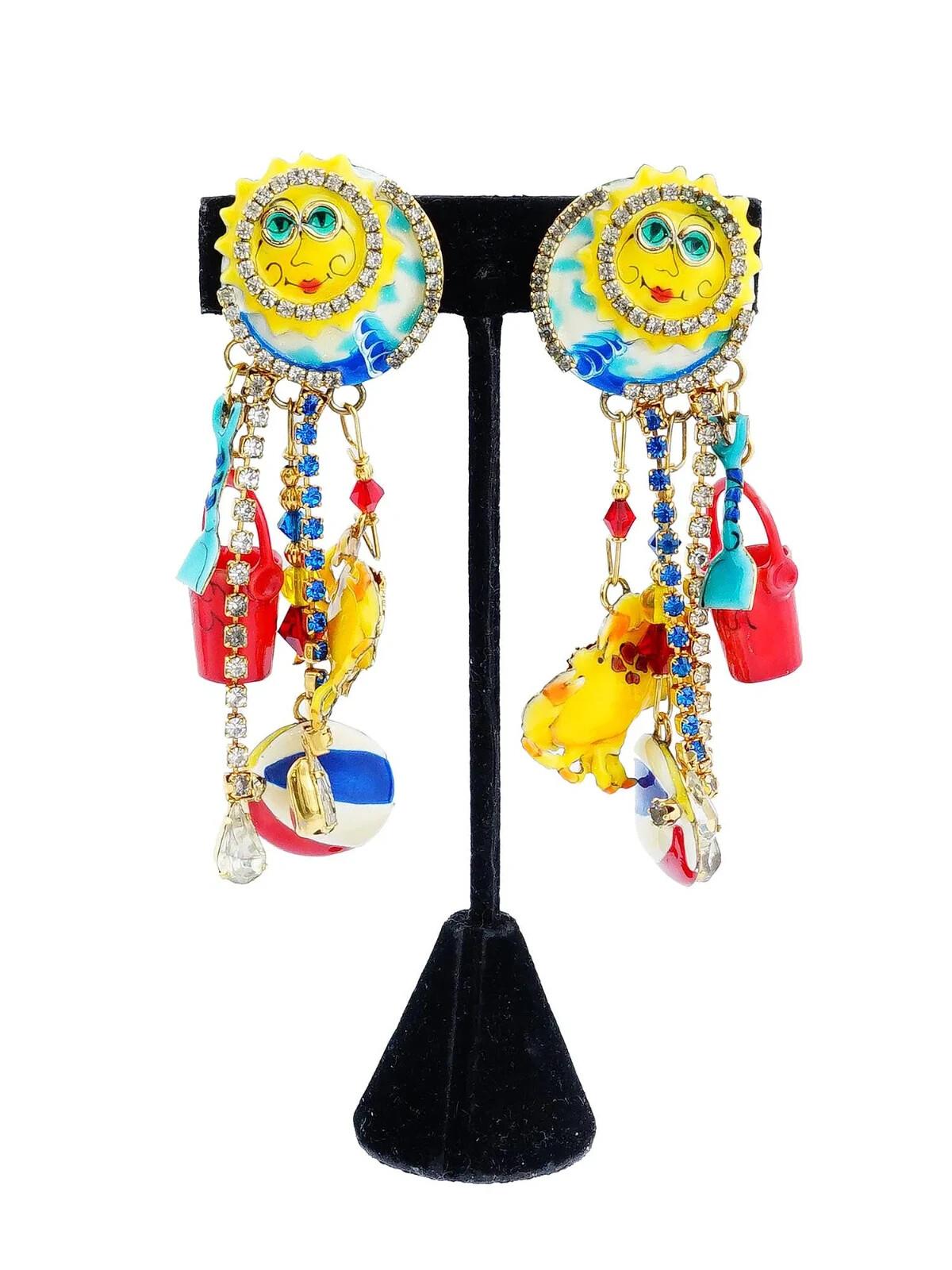 Un paio di orecchini pendenti di bigiotteria Lunch at The Ritz ispirati alle giornate in spiaggia. Gli orecchini presentano motivi di sole giallo brillante ornati da strass. Gli orecchini sono decorati con elementi stravaganti, tra cui charme di