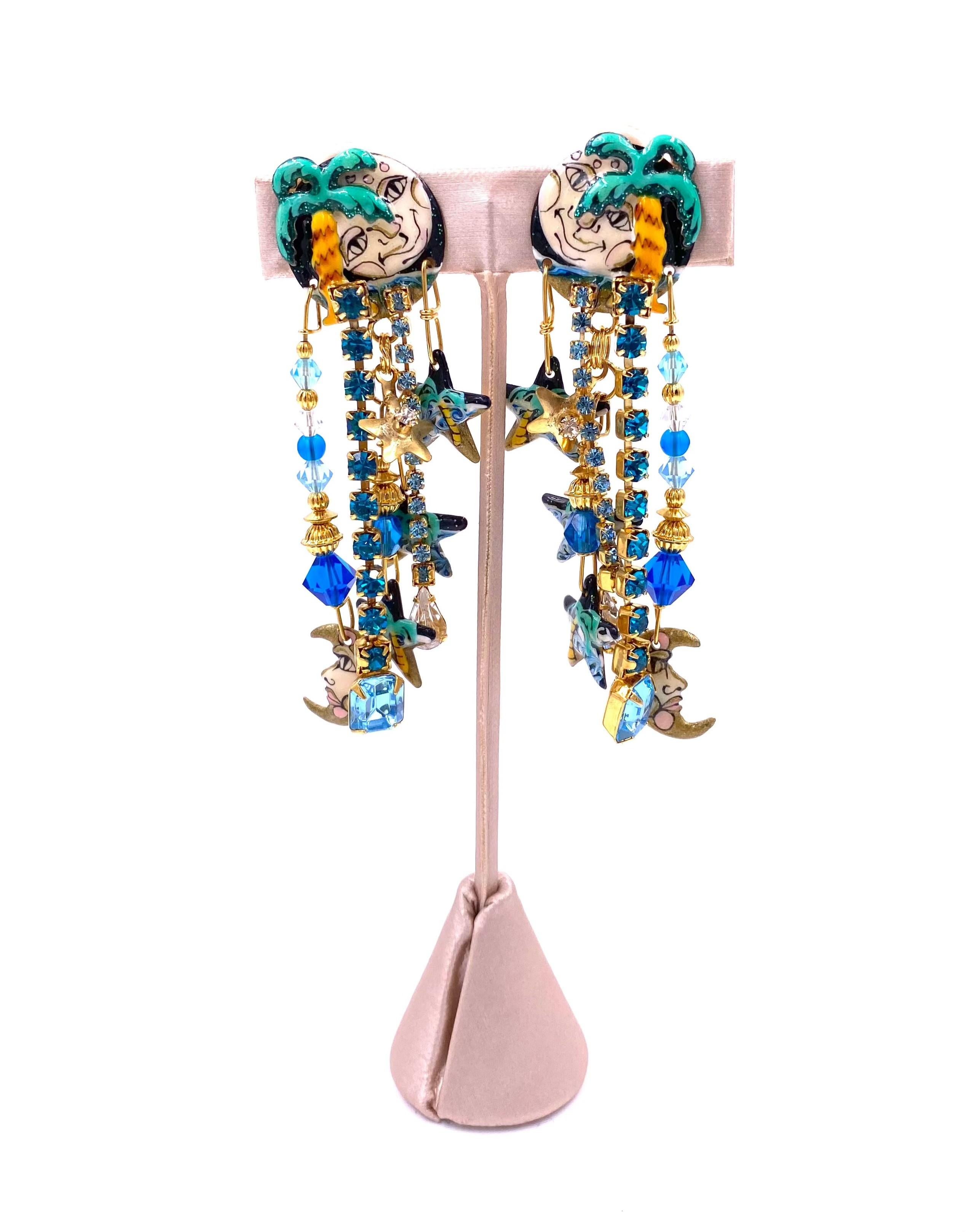 Add a touch of whimsy to your outfit with our Lunch at the Ritz Earrings, Moon Over Miami. Featuring a painted moon and stars detail with blue and gold beading, these dangle earrings are adorned with large rhinestones for an eye-catching look.