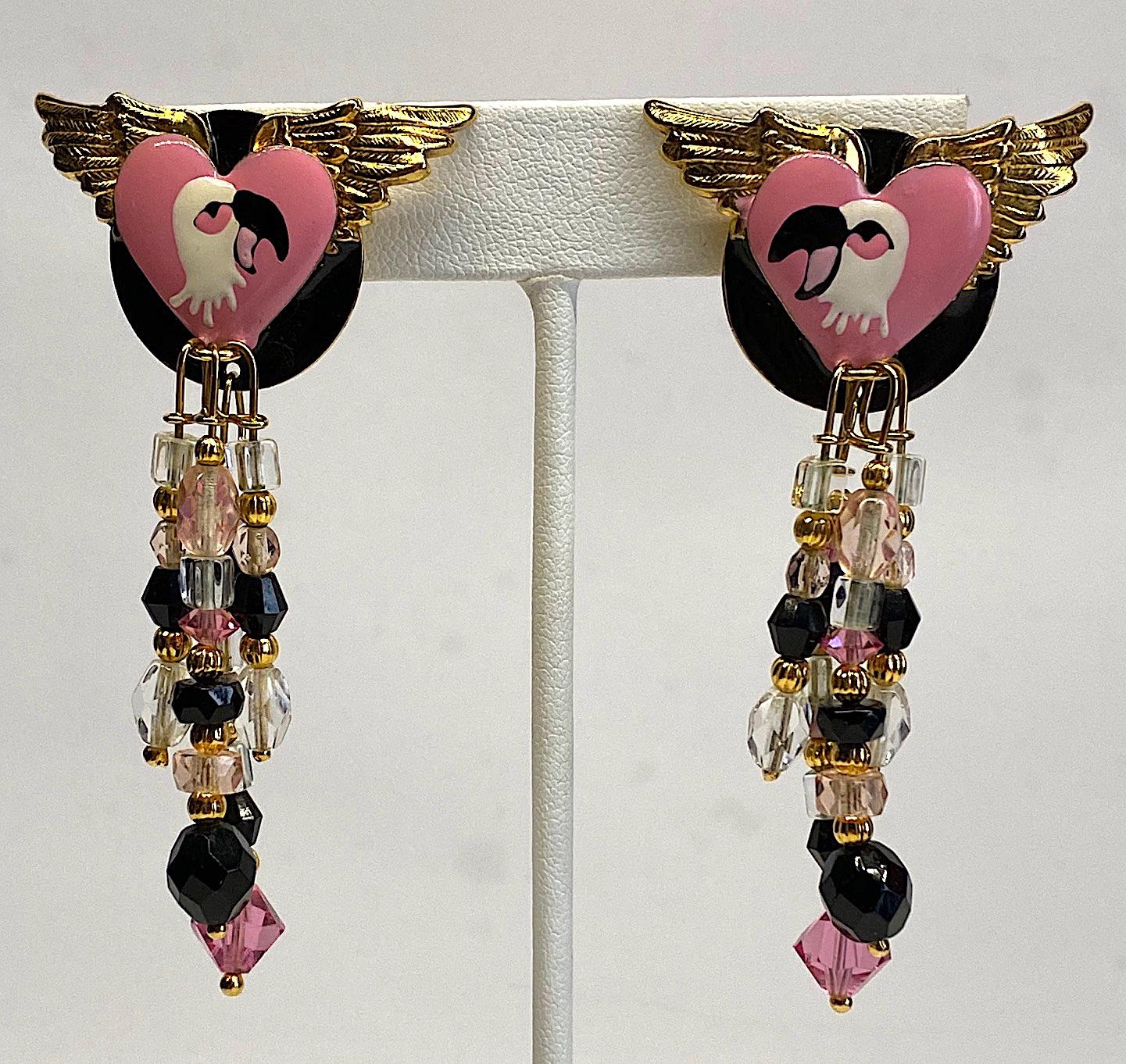 A fun and whimsical pair of Lunch at the Ritz Flamingo theme earrings from 1989. The top piece is comprised of a pink enamel heart mounted on top of a pair of gold wings that are, in turn, mounted on top fo a black enamel disk. The pink heart is