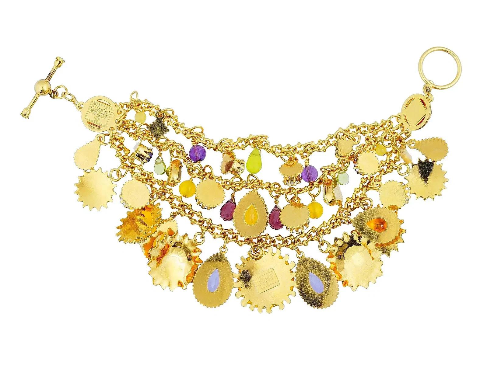 Una pulsera de bisutería Lunch at the Ritz. La pulsera presenta un intrincado diseño adornado con motivos solares, cada uno de ellos elaborado con acentos de color. Una estructura de varias capas que muestra encantos solares dorados. La vajilla está