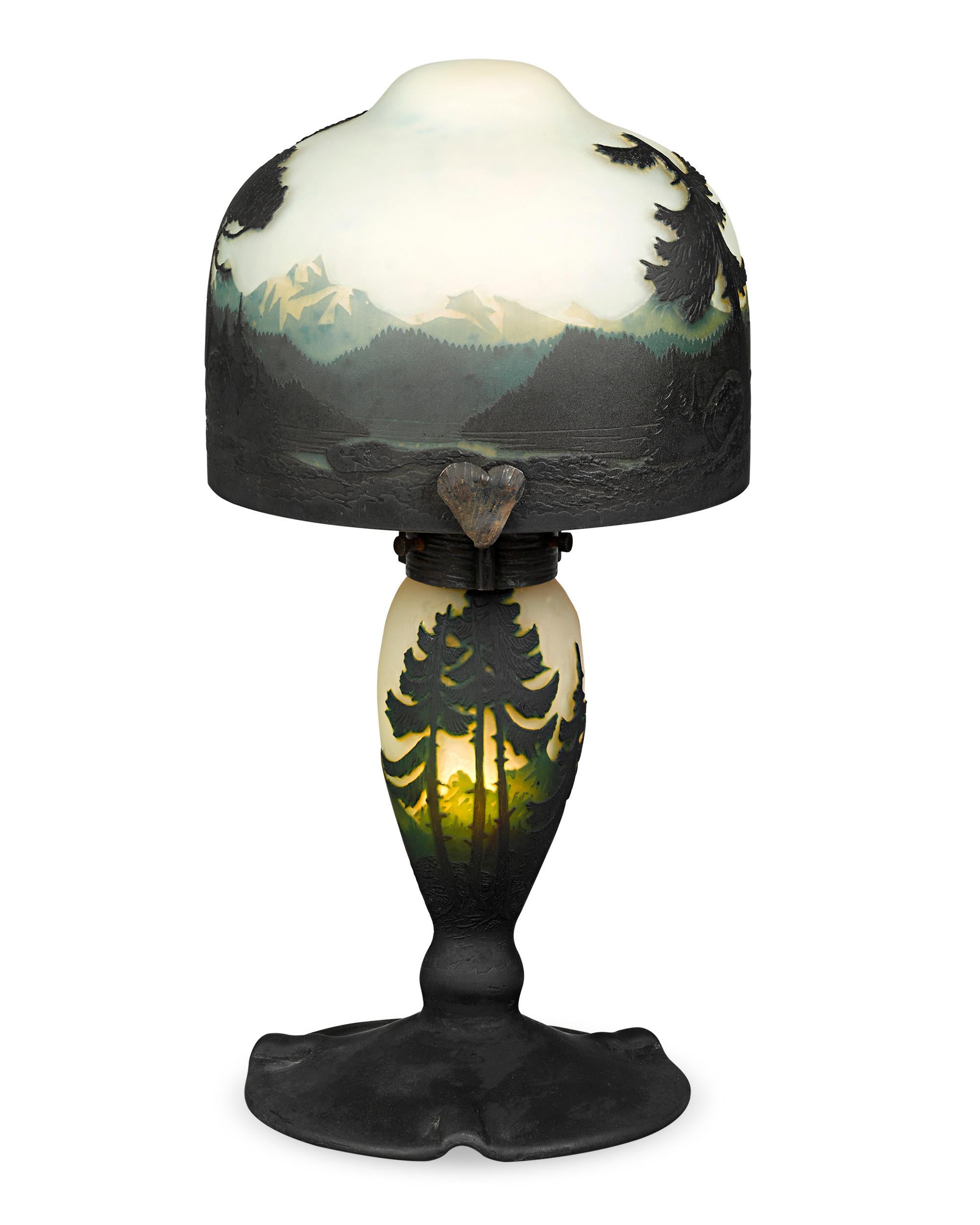 This beautiful cameo art glass lamp is from the acclaimed Muller Frères glassworks and depicts the wilderness surrounding their Lunéville, France studios. Exceptional in its artistry, the lamp casts an alluring glow reminiscent of a hazy morning.