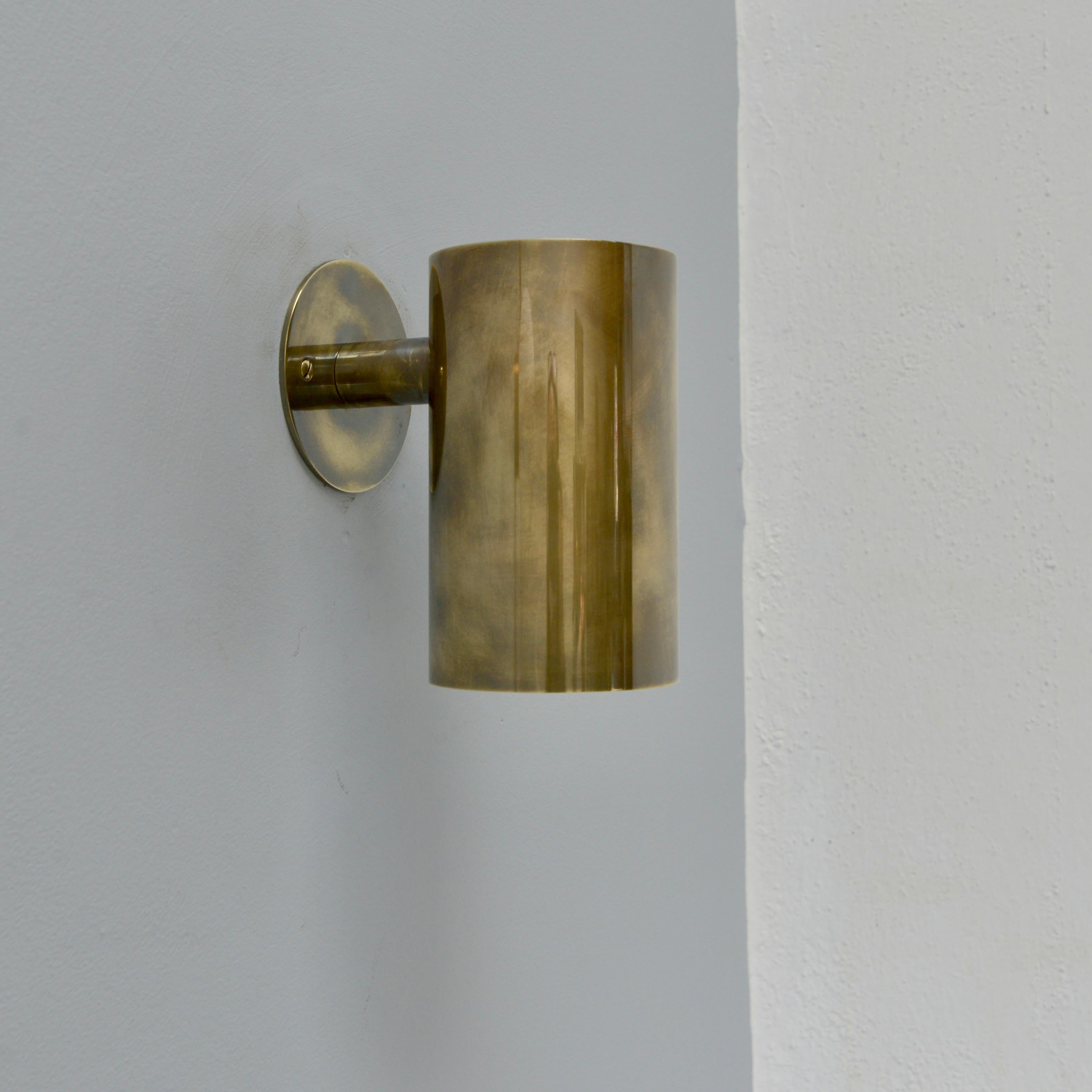 The stunning Lute OD Out/Indoor Sconce by Lumfardo Luminaires is a pure brass cylindrical wall sconce in a patinated un-lacquered brass finish. An all brass fixture, with illumination emitting from the bottom of the cylinder, this sconce is made in