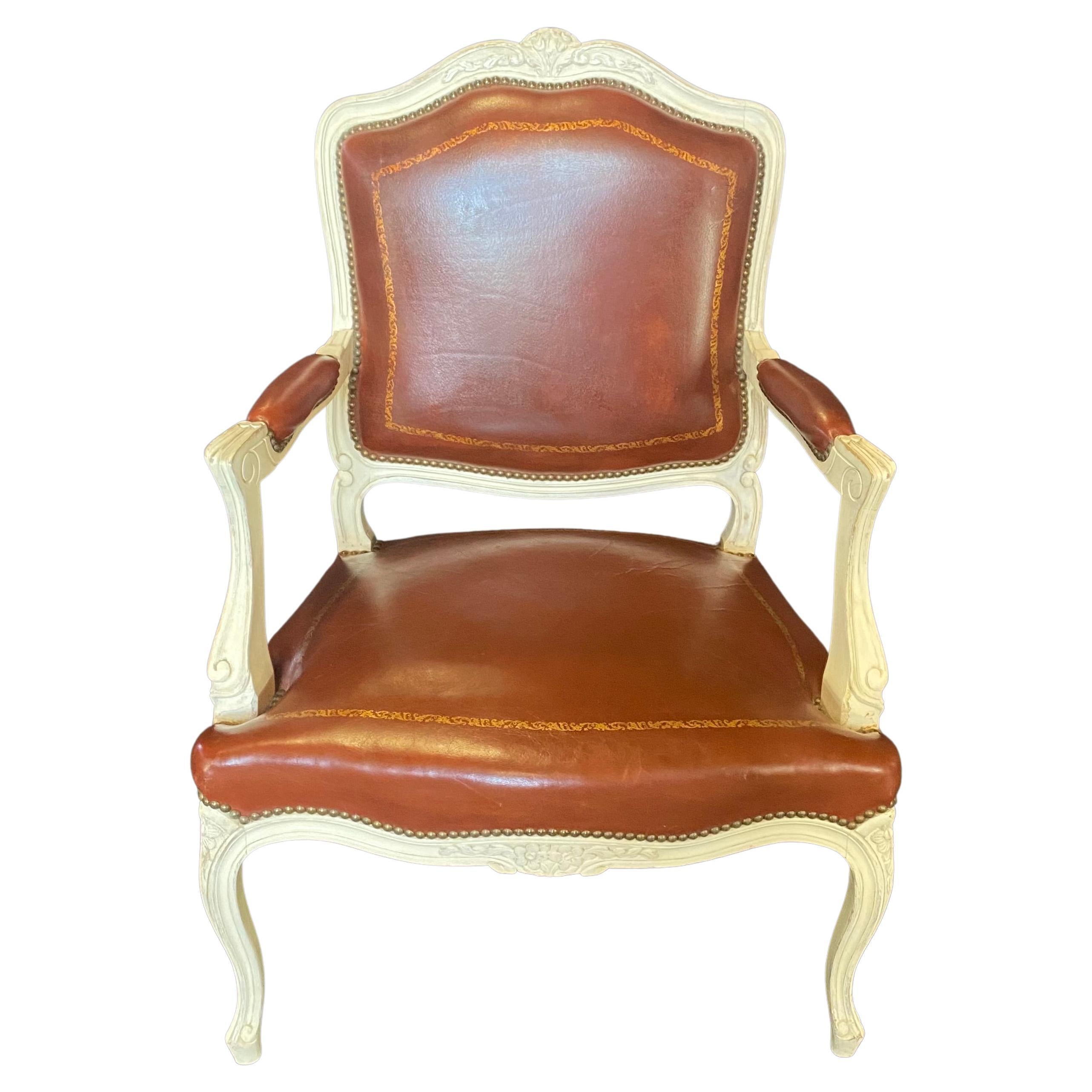 Luscious pair of leather embossed armchairs or fauteuils. Can be used as elegant dining chairs at the head of a table, or armchairs in the livingroom or study. Ivory painted carved walnut provides a lovely background for the embossed brown leather