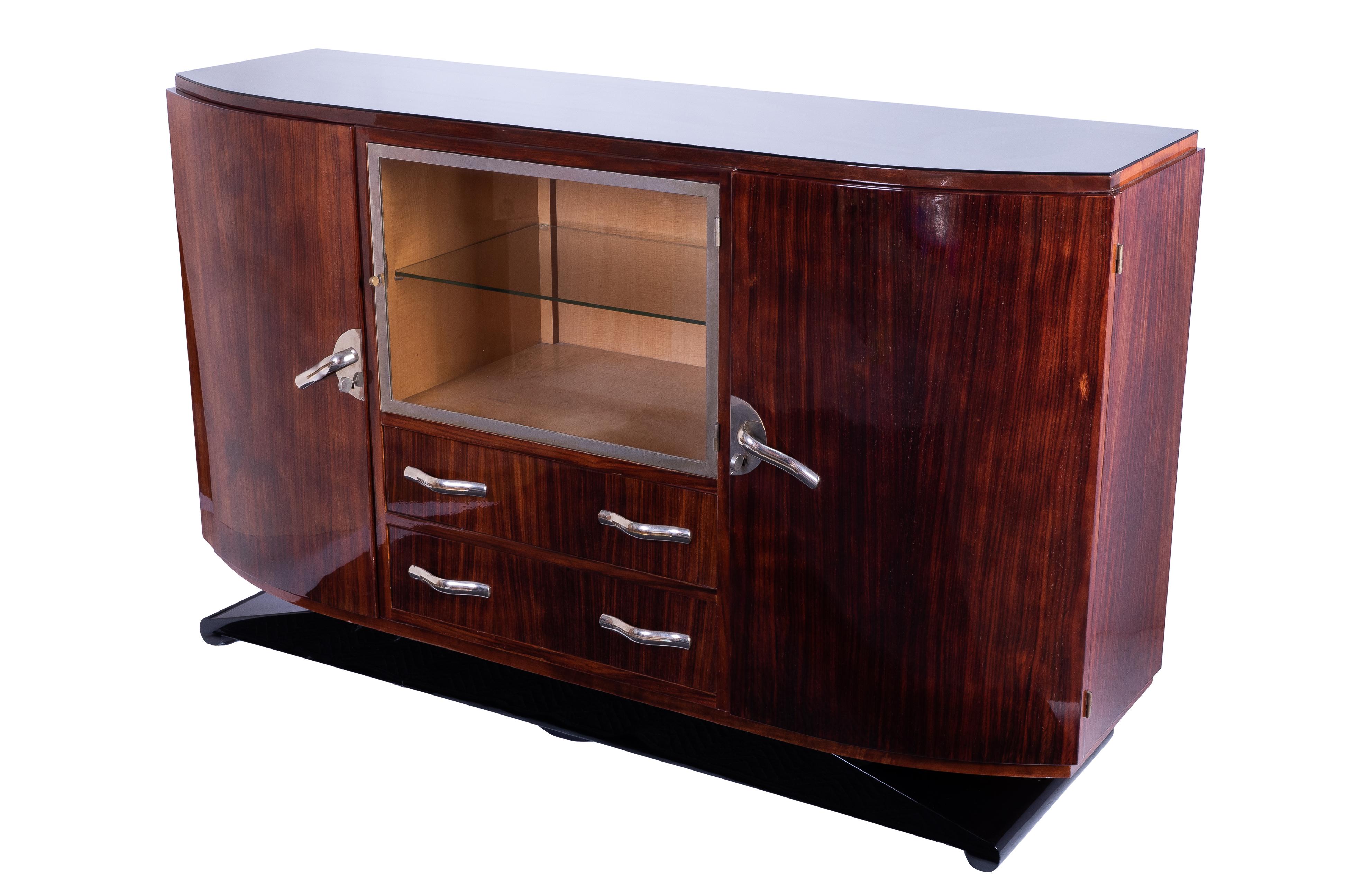 Luxe Art Deco sideboard / credenza / showcase featuring a solid mahogany frame veneered in luxurious light walnut and finished in a high gloss lacquer. The piece has two single side doors, one center display and two center drawers. Plenty of