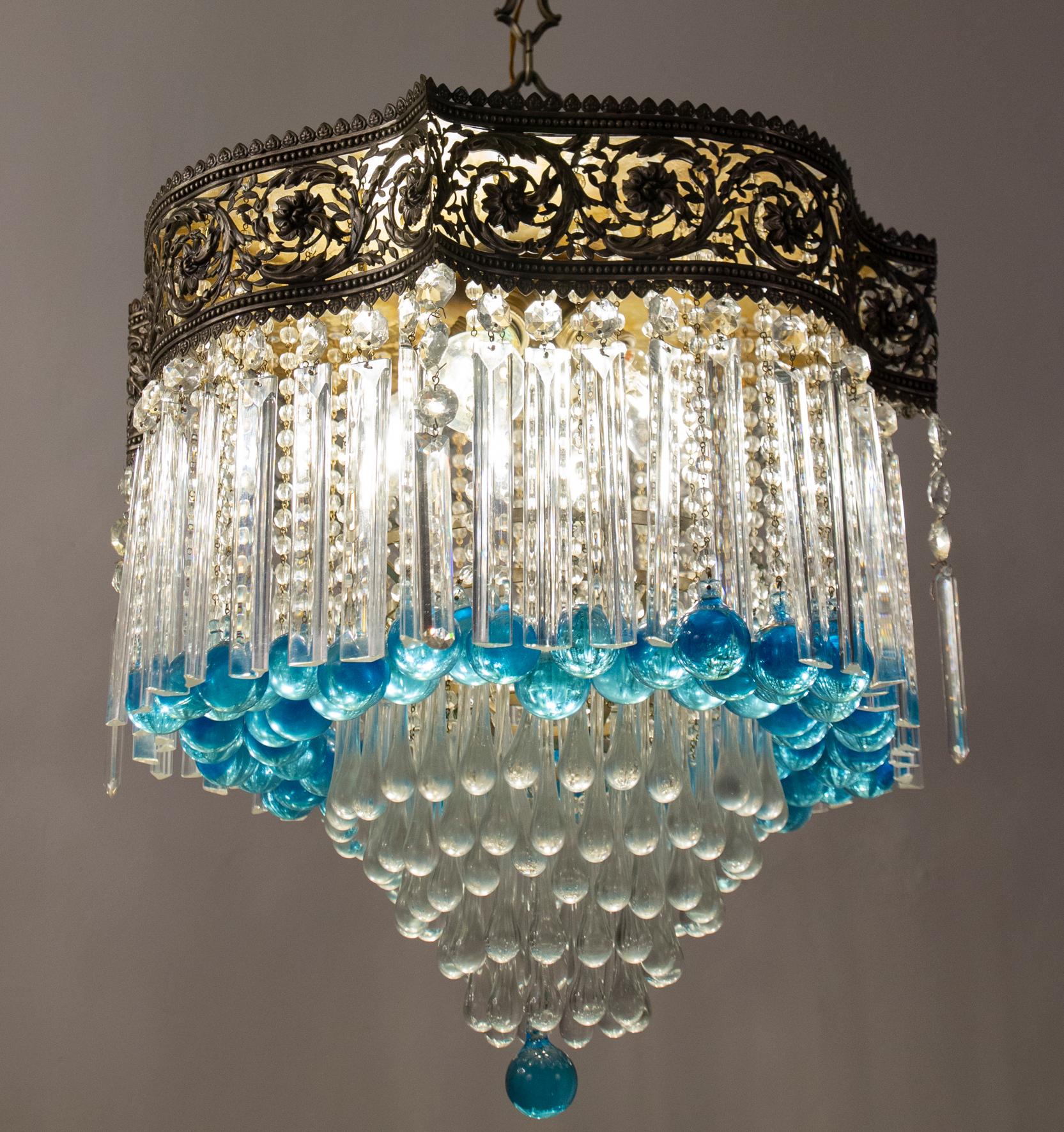 Sontuoso lampadario che sostiene una serie di preziosi prismi di cristallo tagliato e una cascata di gocce blu. . Cornice finemente cesellata di colore argento con ghirlande.
Ideale per una grande sala da ricevimento, una sala da pranzo o un
