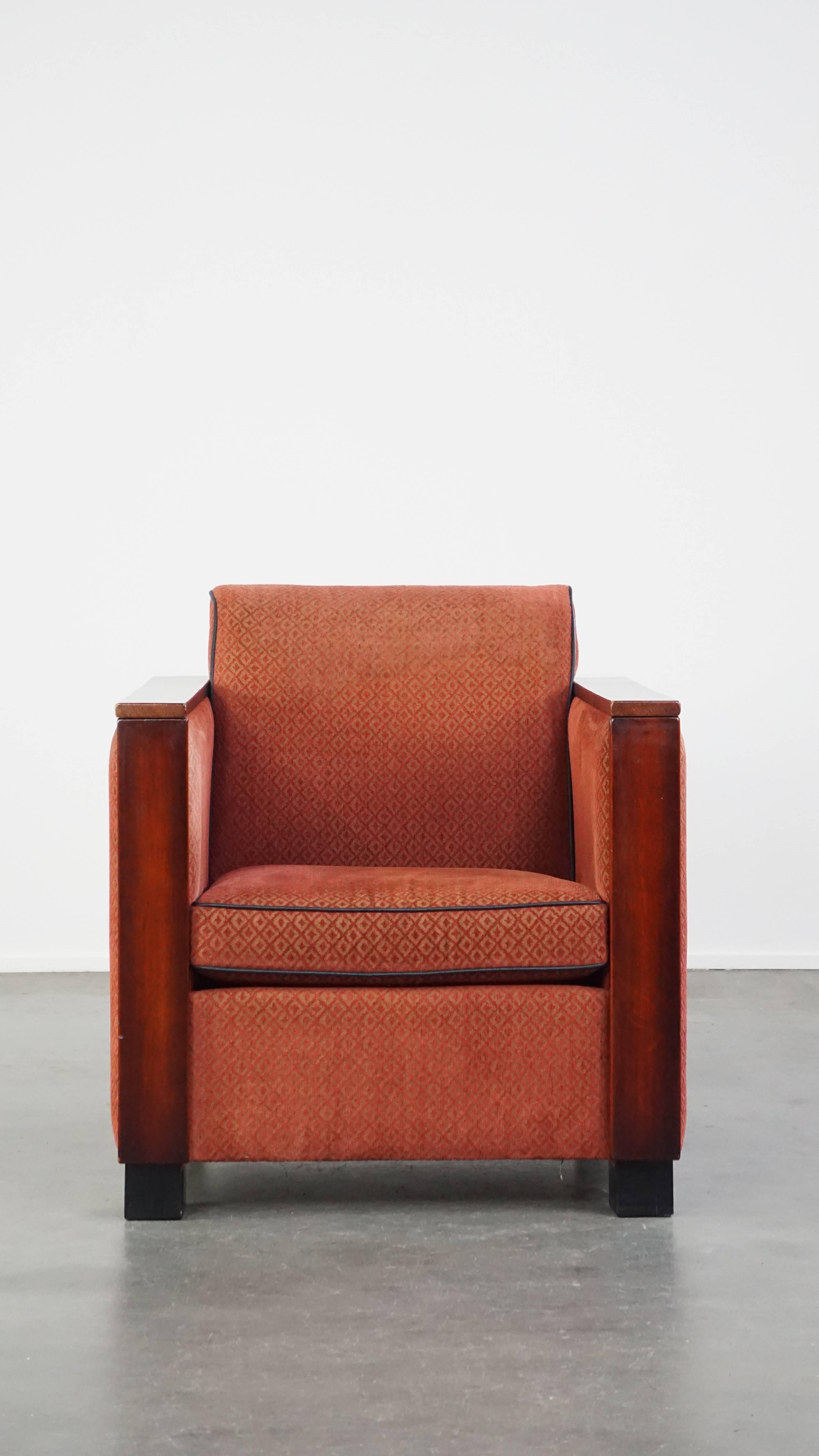 This sleek and luxurious armchair is a true eye-catcher and a great addition for lovers of Art Deco design furniture. It is upholstered in red fabric and features wooden details. The armchair comes with a loose seat cushion and offers the seating