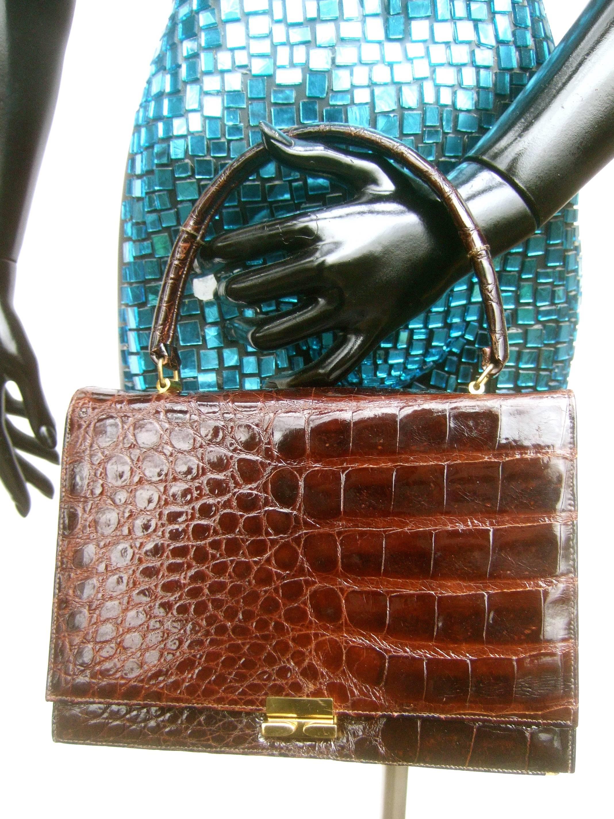 Luxurious brown glazed genuine alligator handbag c 1960s 
The elegant midcentury handbag is covered 
with glossy mahogany brown alligator skin 

The clasp mechanism is sleek brass tone metal 
The interior is lined in light tan leather designed 
with