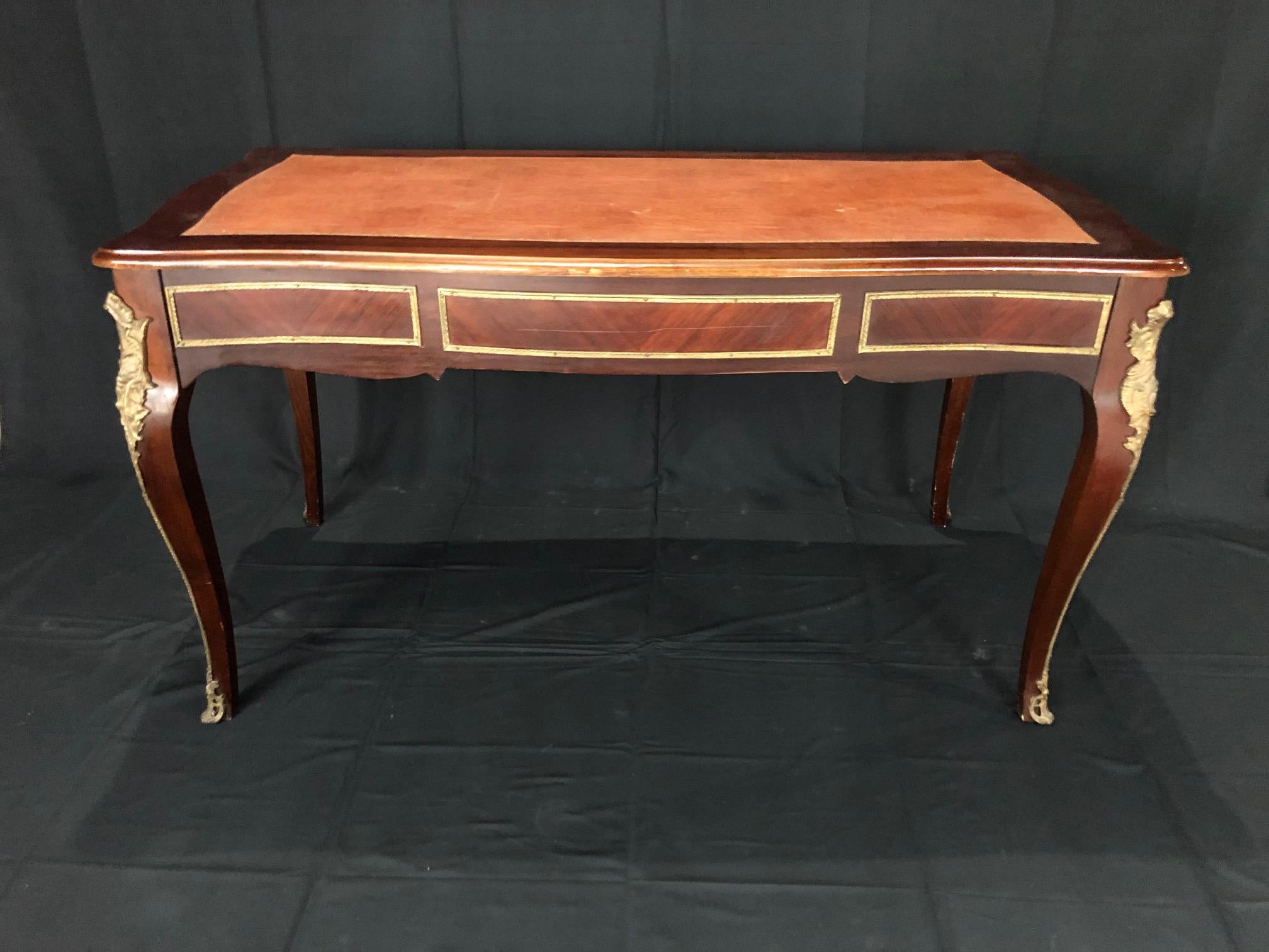 French Louis XV style walnut and ormolu bureau plat desk raised on elegant cabriole legs, dressed in ormolu wraparound sabot. The 3 drawers are decorated with gilt bronze handles, bronze detailing, and a central key hole escutcheon. The back is