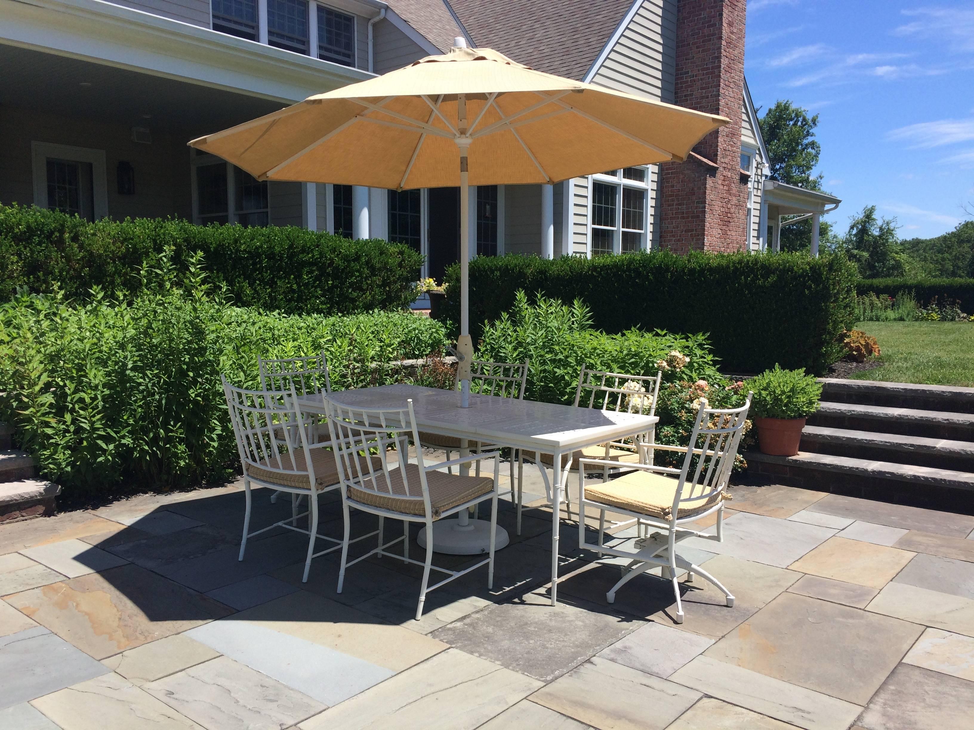 Stunning large rectangular outdoor dining table and six matching chairs in white cast aluminum, having very large umbrella and custom seat cushions upholstered in Sunbrella. The two chairs at the head swivel.  Summer Classics. Windham