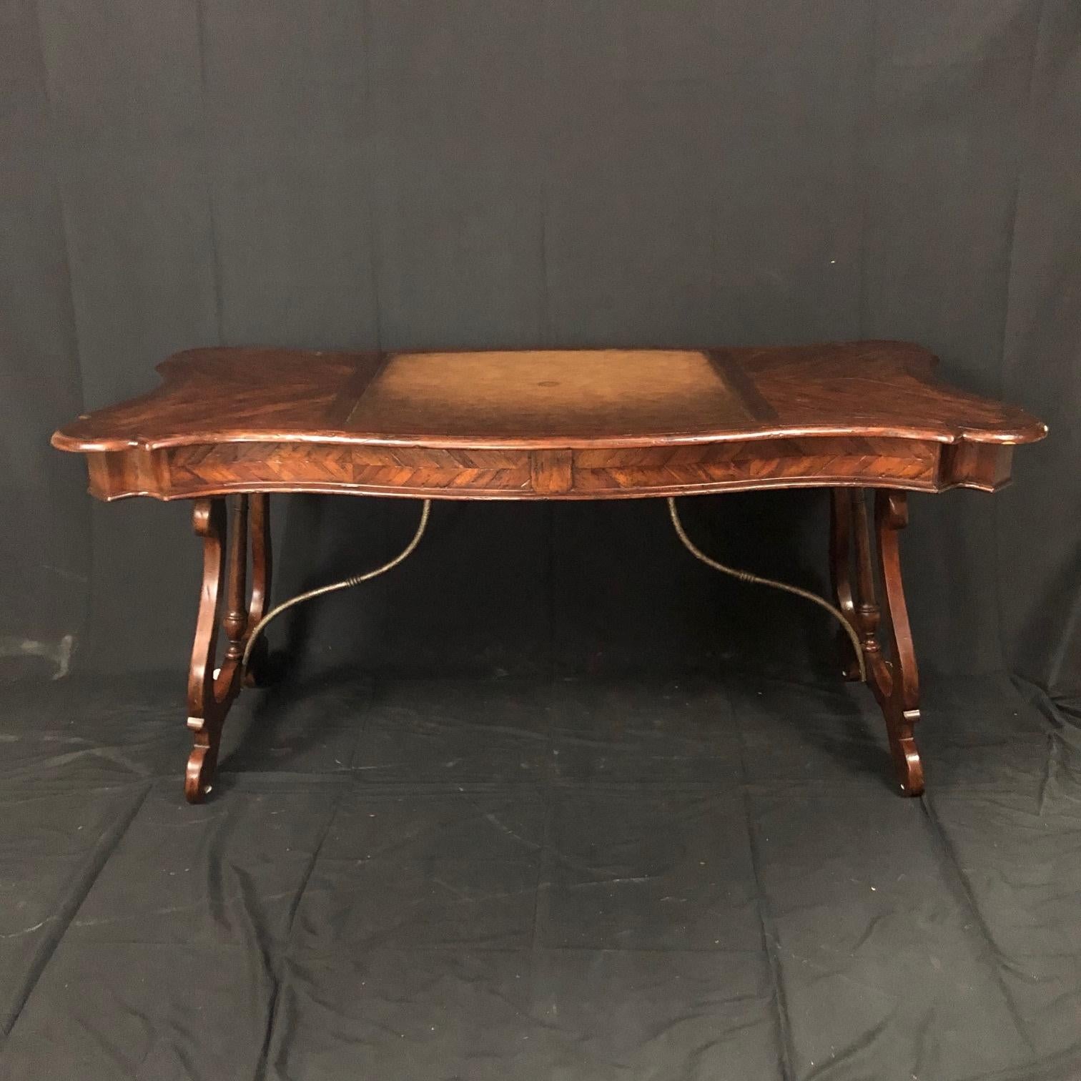 An antiqued mahogany writing table, desk or bureau plat having serpentine parquetry planked top inset with a central burnished and hand tooled leather writing surface above two frieze drawers, on splayed lyre supports with a baluster turned central