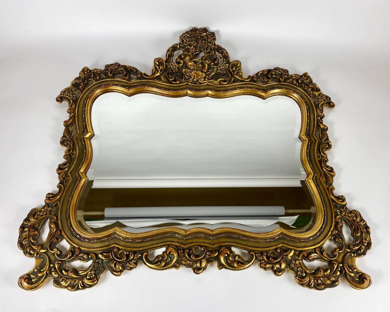 Vintage carved giltwood mirror, Mid-20th century.

Faceted wall mirror with golden rectangular ornate Baroque frame. Perfect for over-console bedroom, foyer or living room.

The rectangular shaped mirror with pierced scrolled acanthus cresting