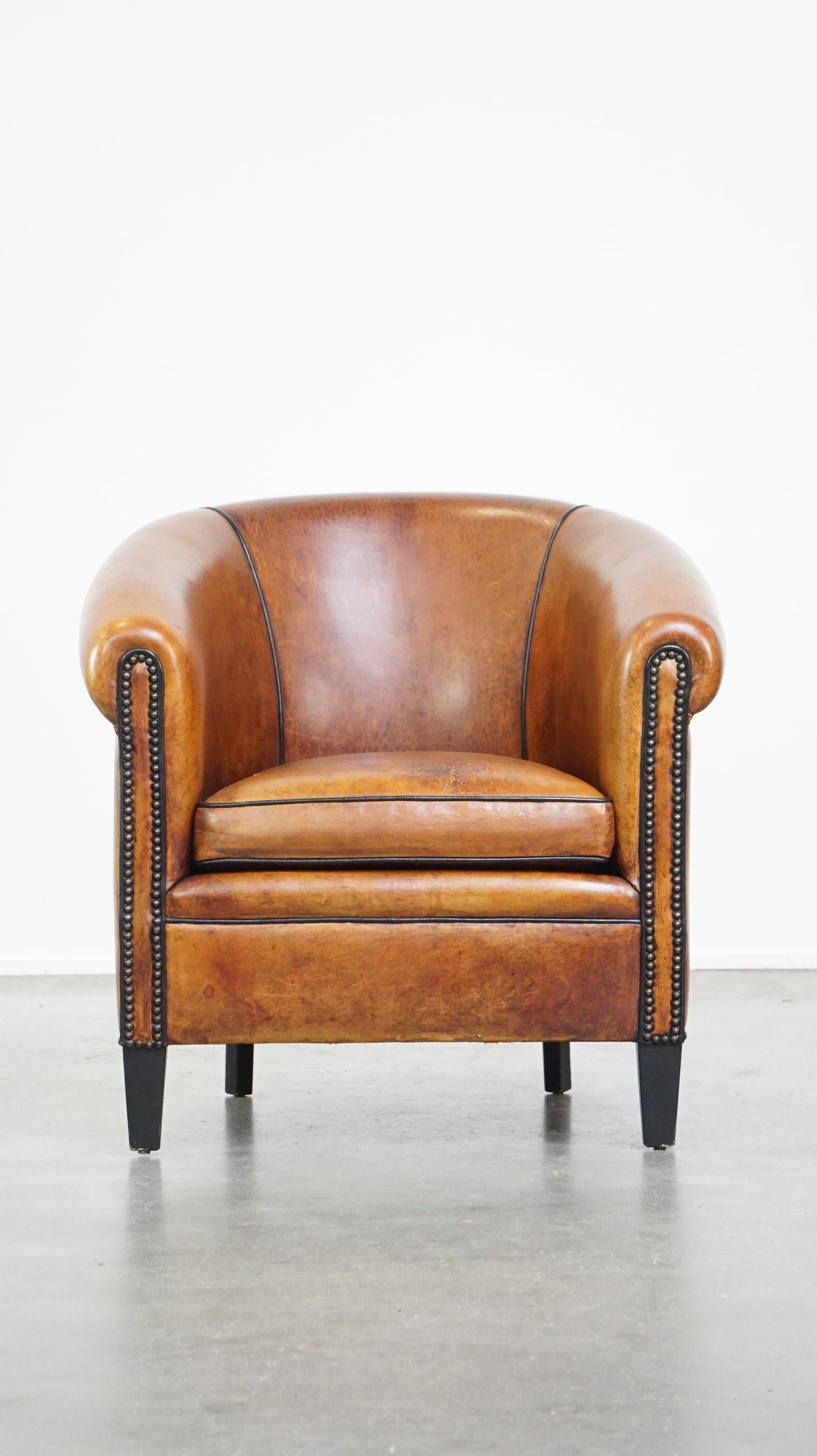This rugged sheep leather club armchair is luxuriously finished with black piping and decorative nails. It is of excellent quality, and despite its bold appearance, it is still as comfortable as can be. Due to frequent use, it shows signs of wear
