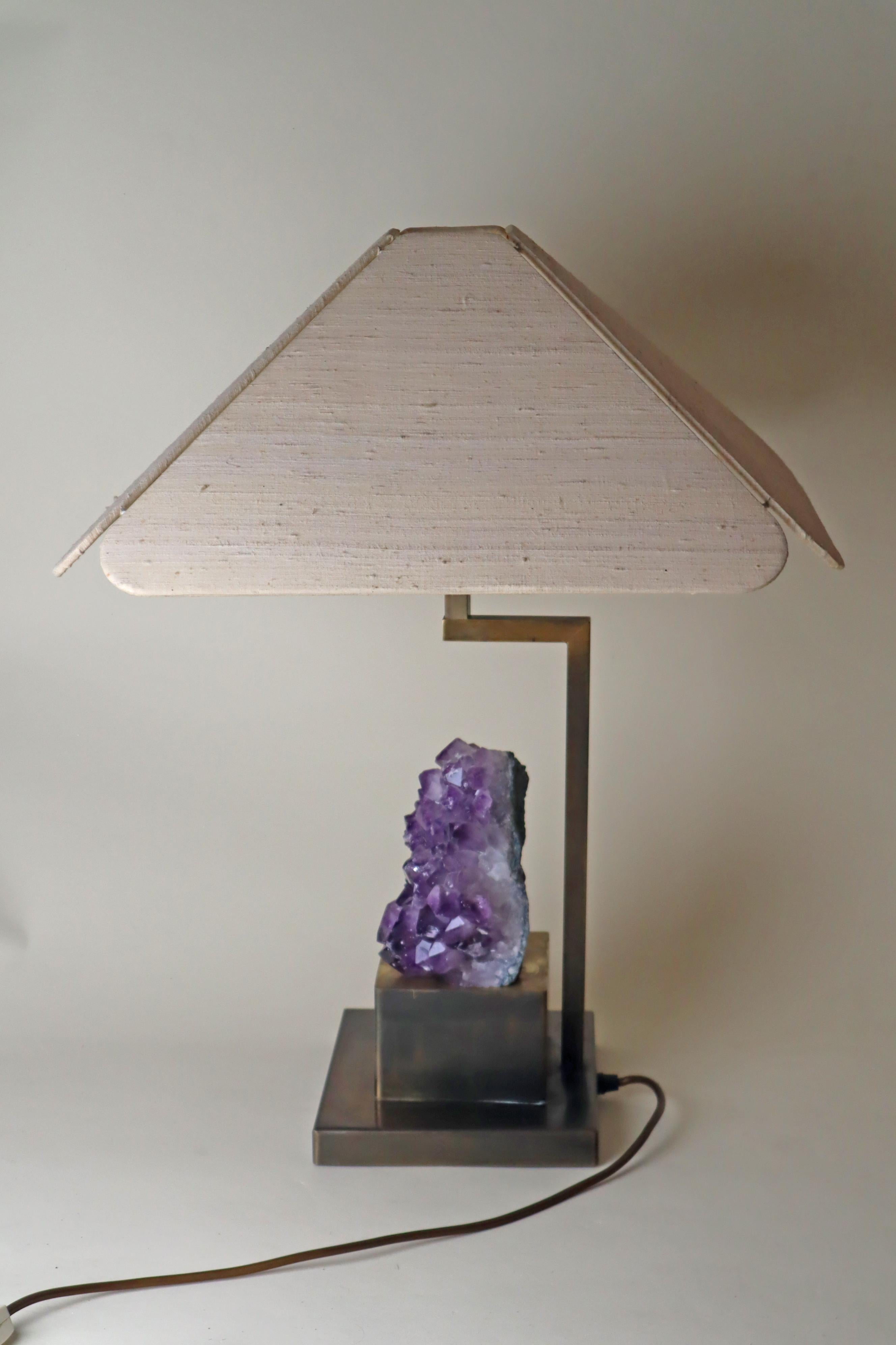 Cette magnifique lampe de table est une pièce de créateur unique. La particularité est que la grande et belle améthyste violet foncé peut être éclairée de l'intérieur, ce qui place la pierre dans une lumière particulièrement belle. Le cadre de la