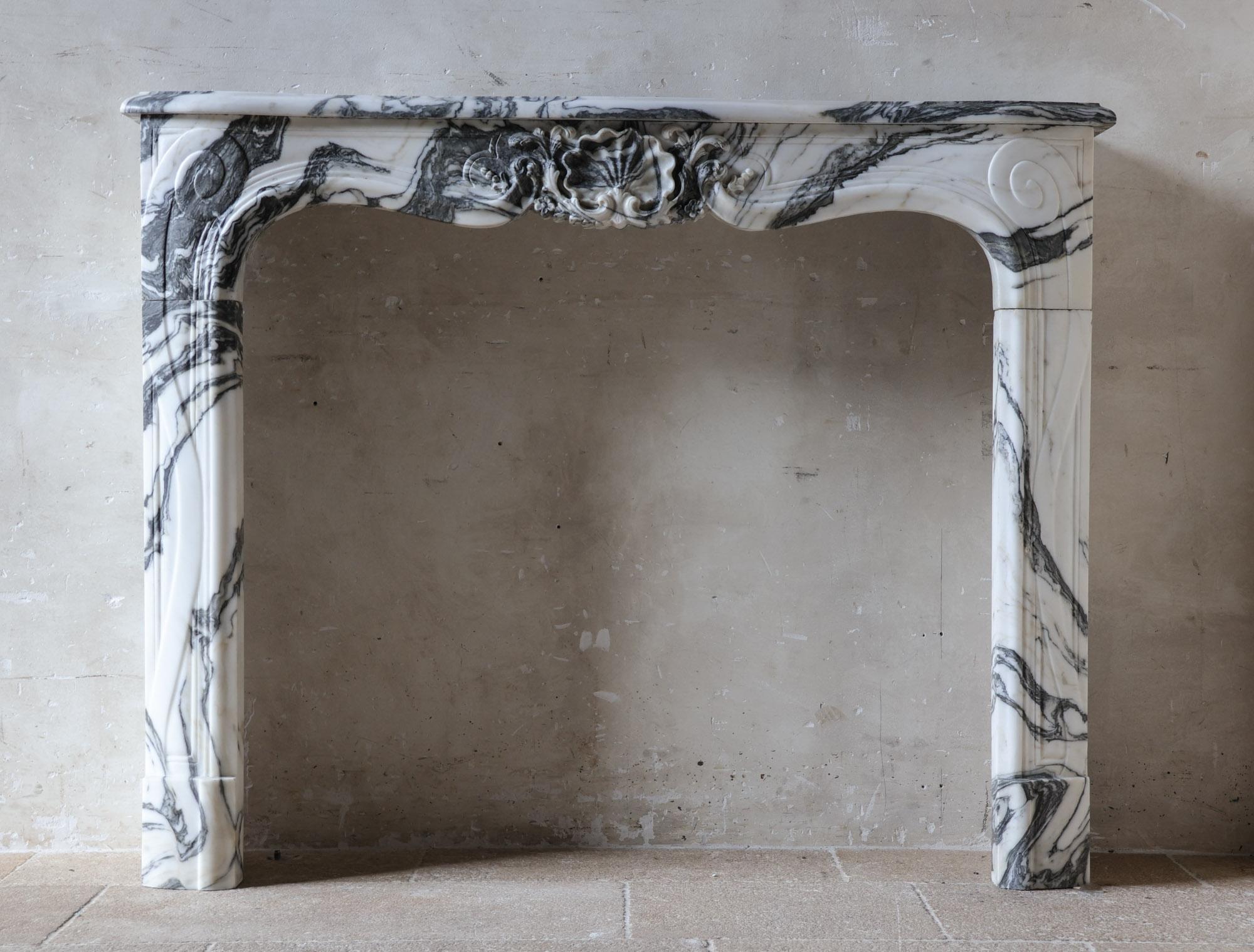 Dieser atemberaubende, luxuriöse, antike Kaminsims wurde fachmännisch aus großporigem Calacatta-Marmor gefertigt, der für seinen satten weißen Hintergrund und seine ausdrucksstarke graue Aderung bekannt ist. Das Ergebnis ist ein dynamischer,